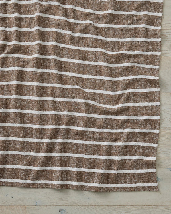 Taupe and cream striped throw draped on whitewashed timber, featuring wavy horizontal bands and linen texture for coastal-inspired home styling