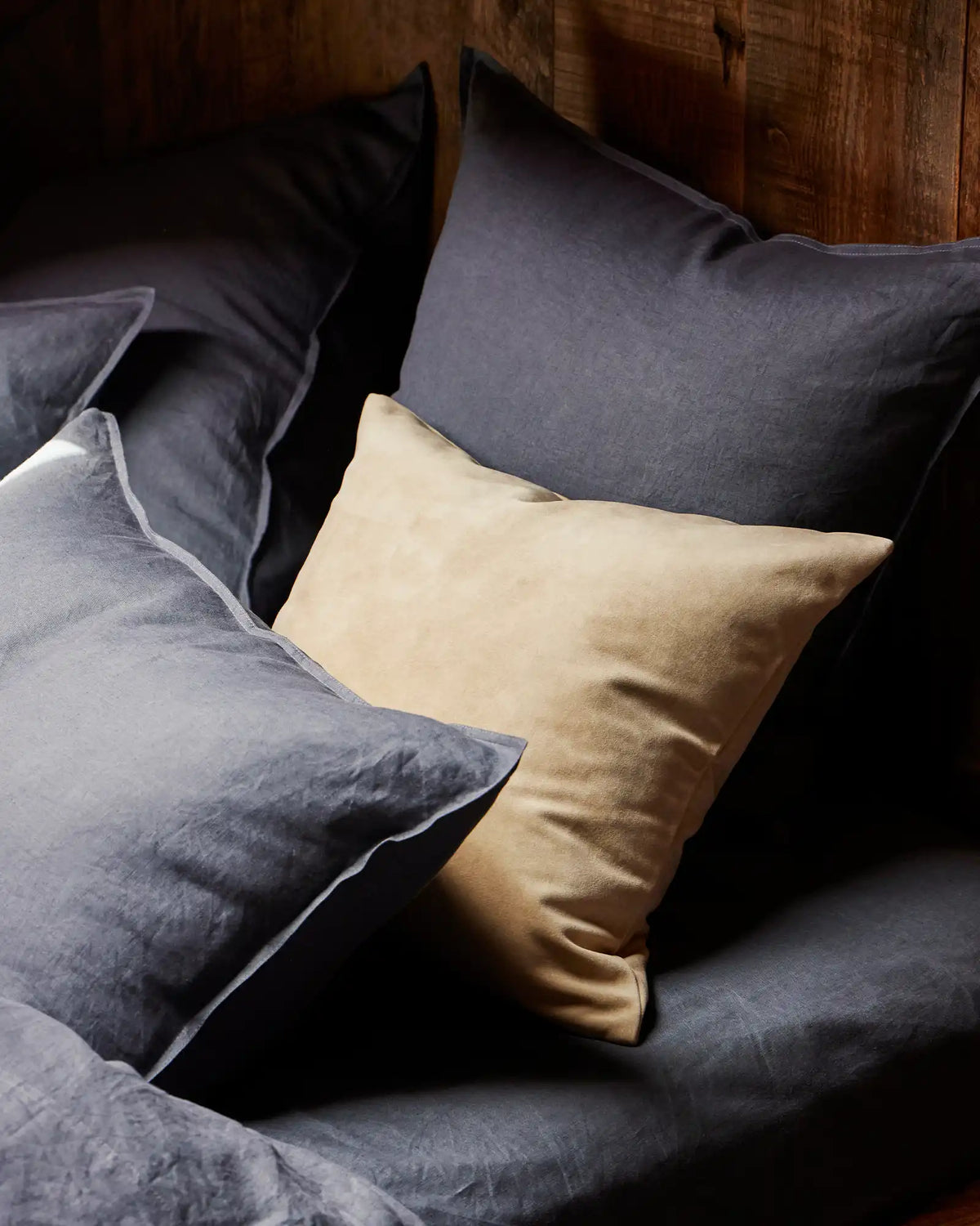 Layered bed styling with Ravello Fitted Sheet and Ravello Pillowcase in denim, cream, and charcoal linen tones against warm timber headboard