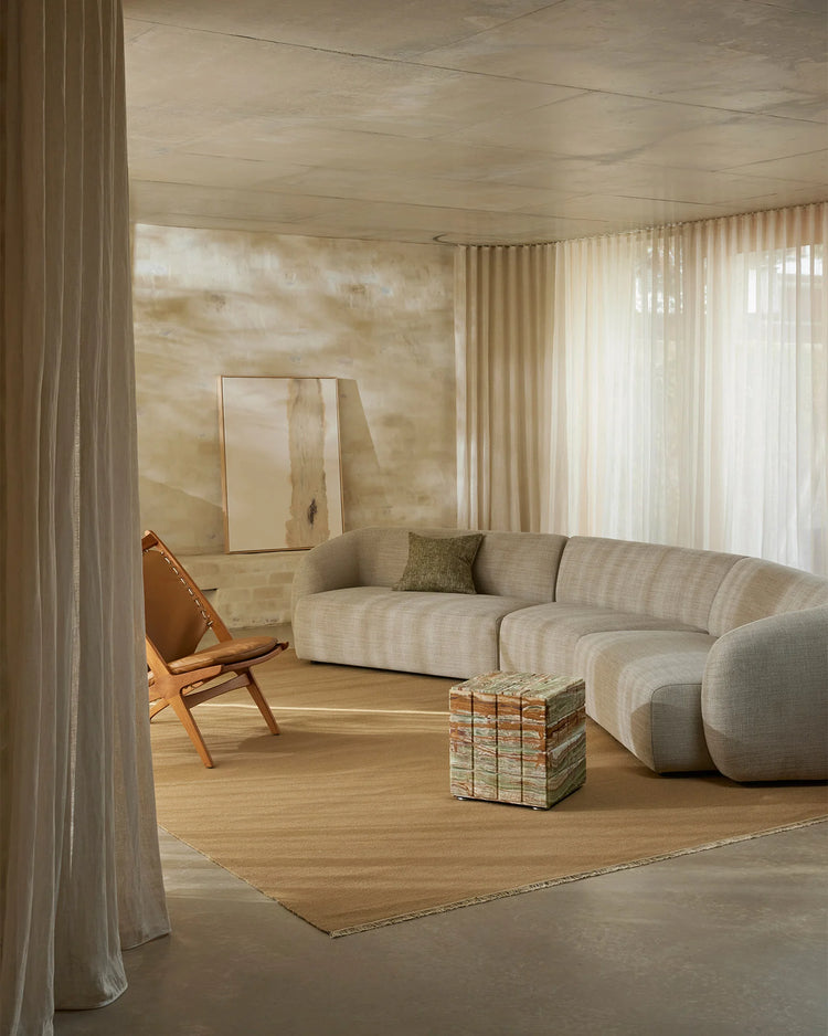 Minimalist living room with neutral linen sofa, warm wood flooring, and Jacqueline rug in natural tones, styled with caramel leather chair and sheer cream curtains