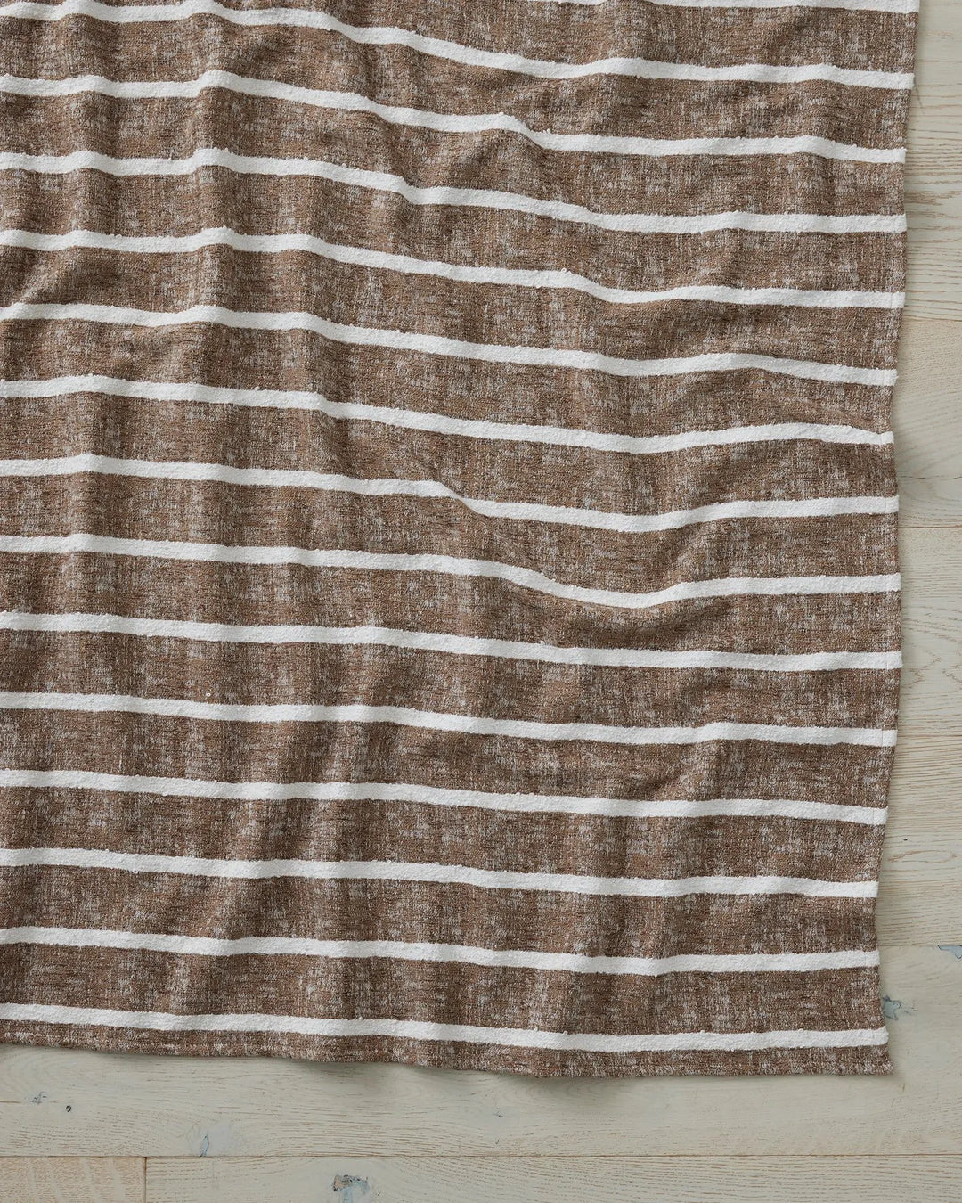 Taupe and cream striped throw draped on whitewashed timber, featuring wavy horizontal bands and linen texture for coastal-inspired home styling