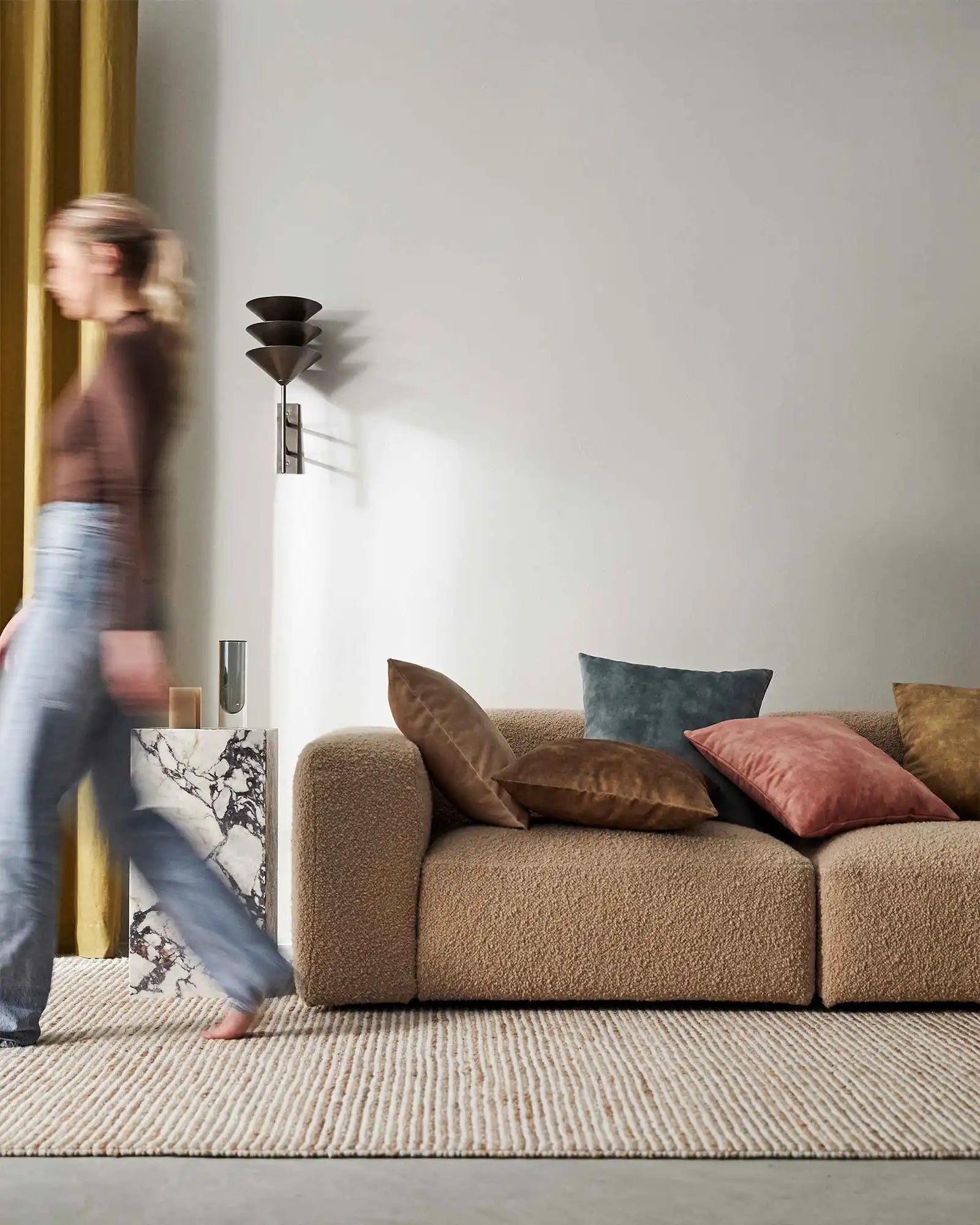 Warm neutral living room with textured beige sofa styled with terracotta, brown and teal Ava cushions, gold curtains, and natural linen rug in earthy palette