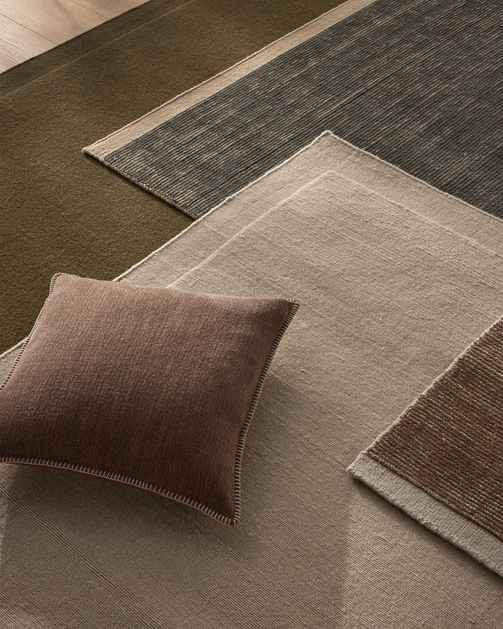 Earthy toned interior styling with Cassio Fog rug, Alba cushion and layered natural textiles in sage green, warm taupe and charcoal with prominent linear weave textures