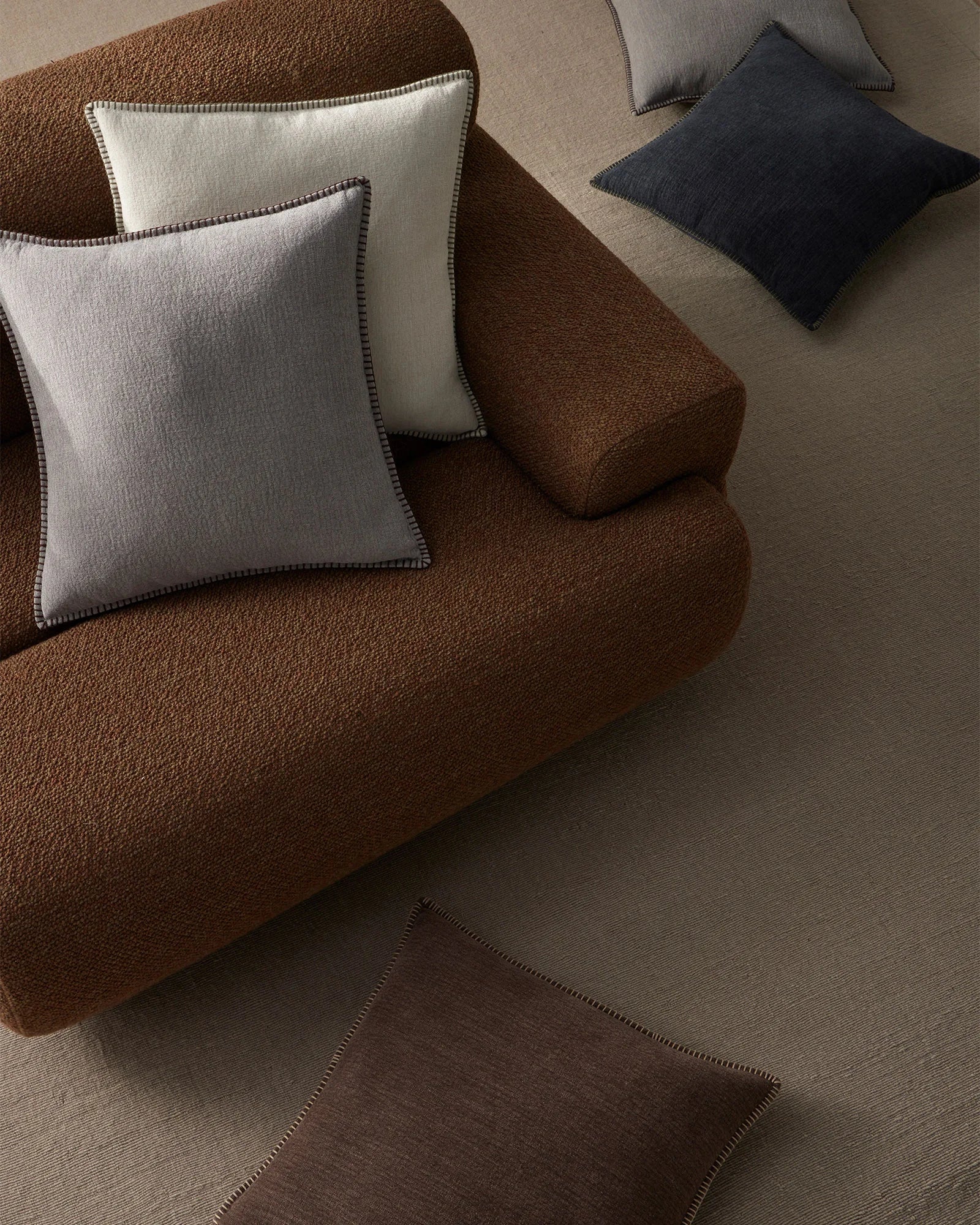 Neutral living room styled with chocolate brown sofa and cream Alba cushions with blanket-stitch detailing, navy and taupe accents on warm beige flooring