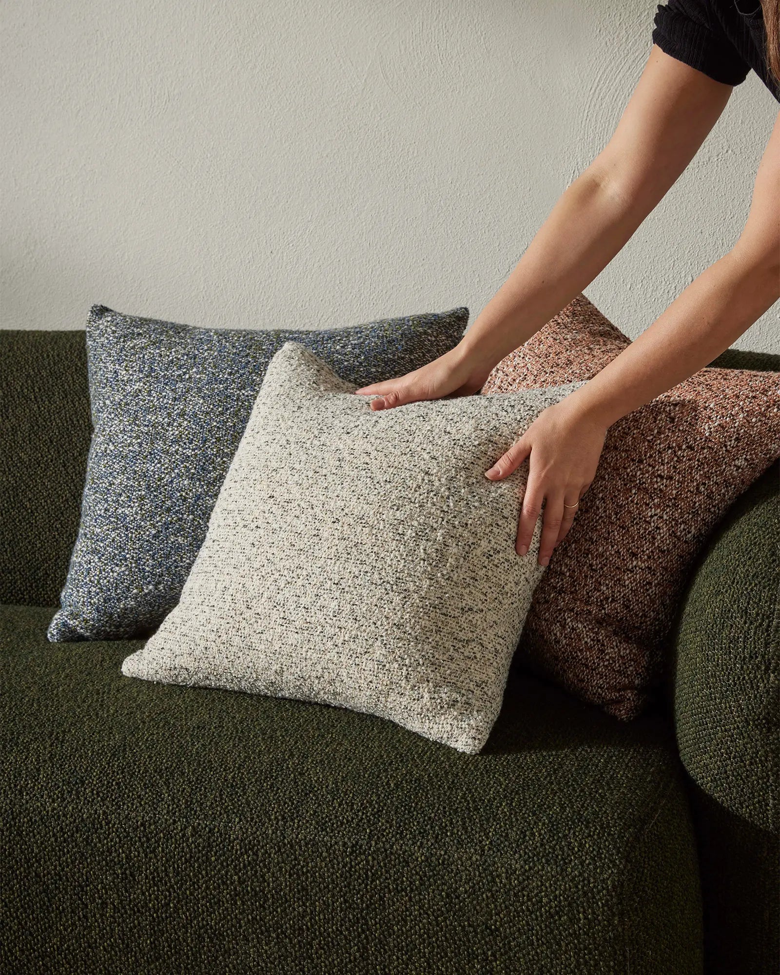 Earth-toned cushion collection in charcoal, cream and terracotta displayed on a sage upholstered sofa, showcasing textured woven fabrics in warm and cool neutrals