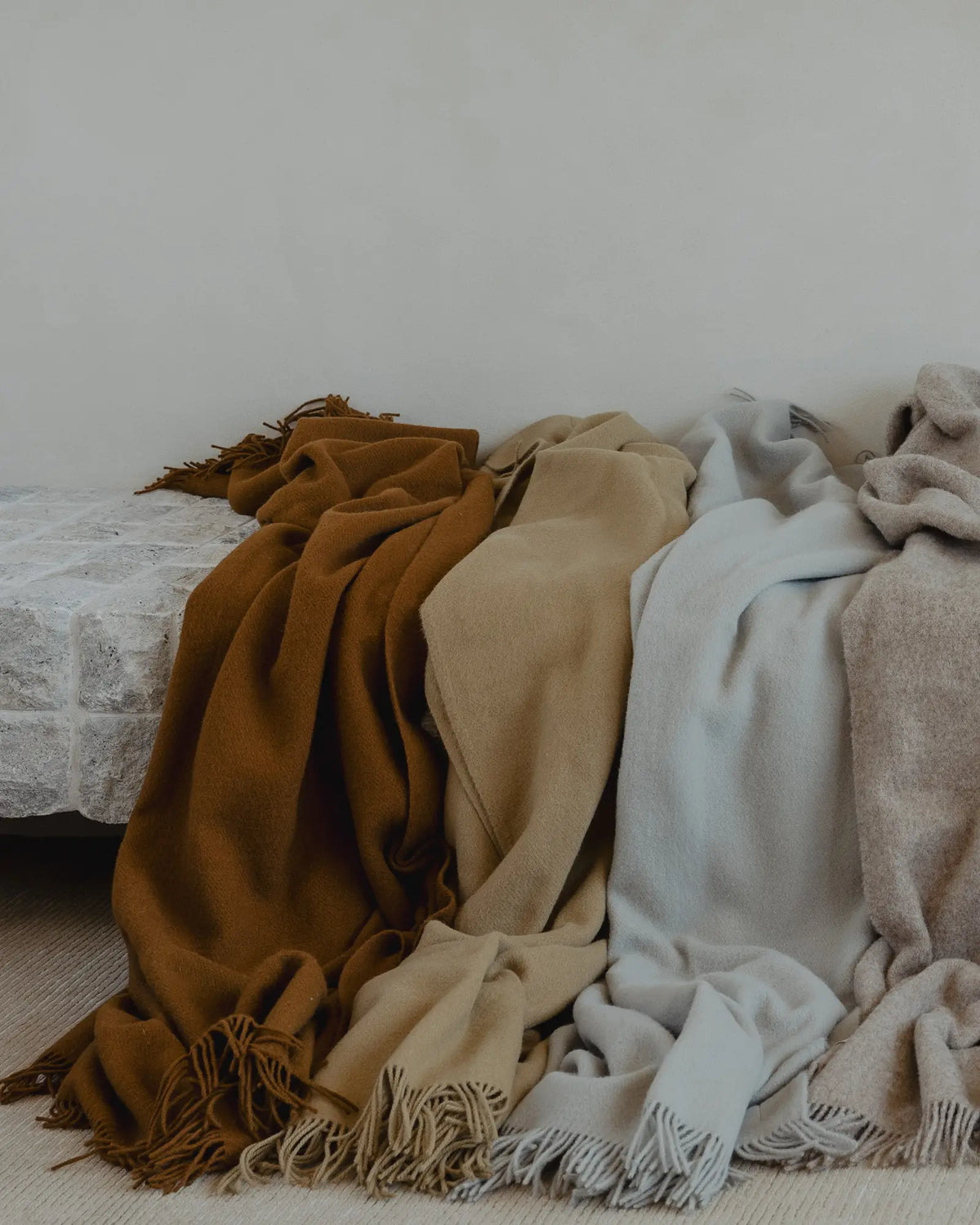 Nevis Camel lambswool throw in warm biscuit brown, displayed with coordinating neutral wool throws, tassel borders visible by Weave Home