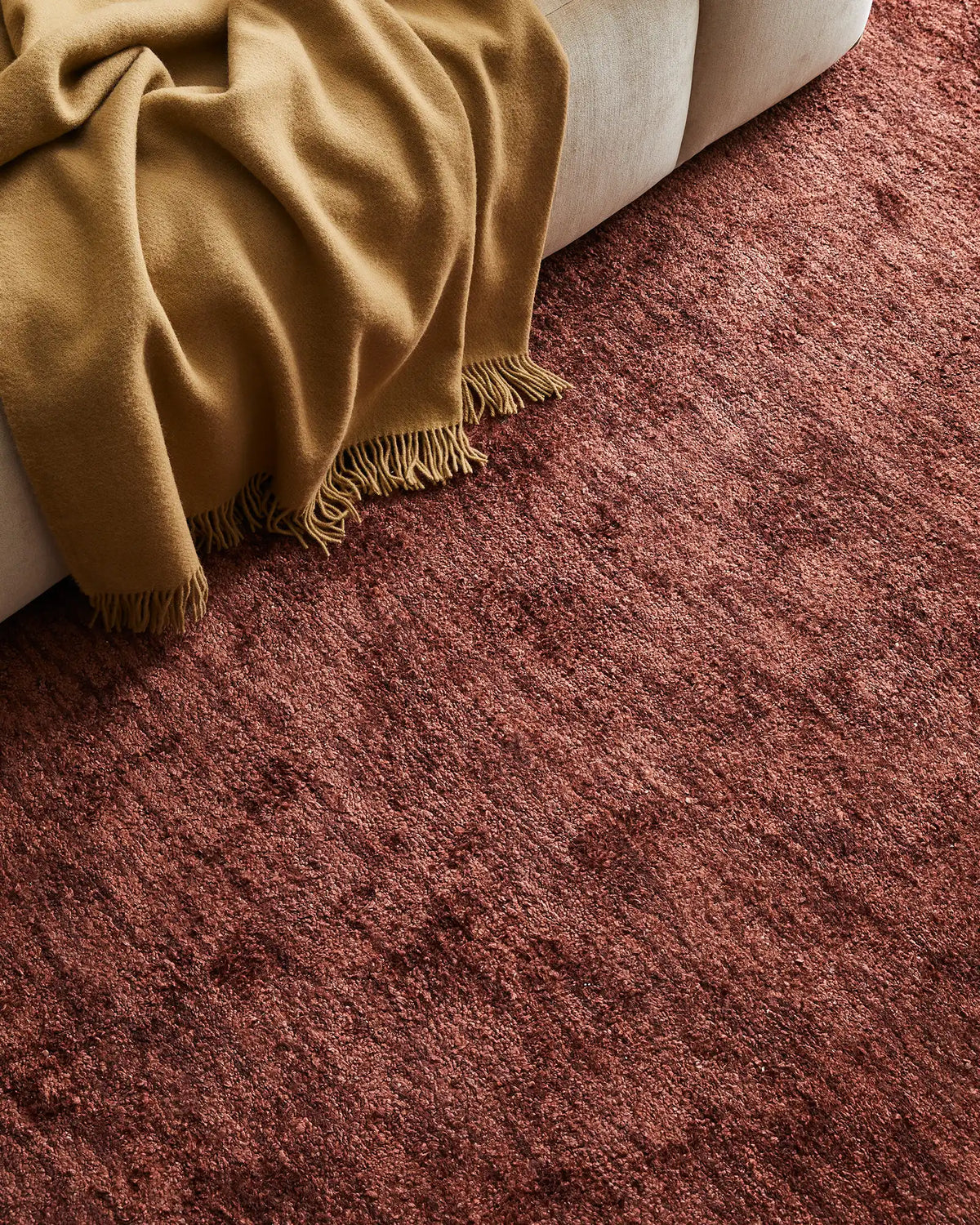 Warm earthy tones of mustard and terracotta create a cohesive interior mood, with a fringed wool throw draped over cream upholstery and a textured bamboo silk rug anchoring the layered seating arrangement.