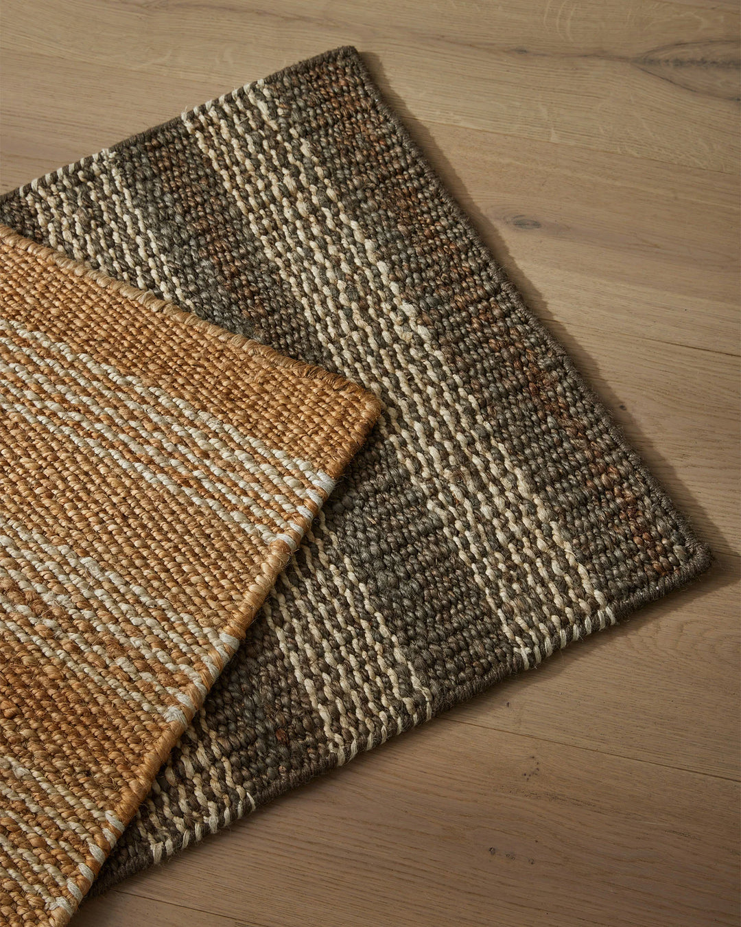 Arden door mats in natural and charcoal tones layered on light wood flooring, showcasing woven jute texture and neutral earthy palette