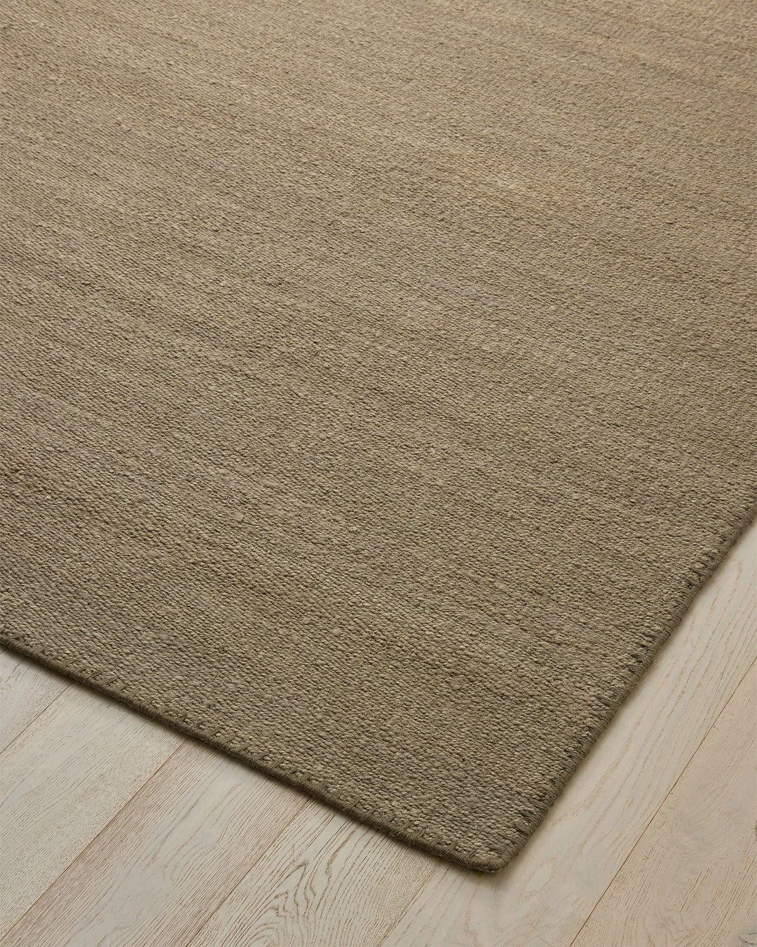 Monroe Flint high traffic rug in soft earthy green with blanket stitch border detail, three-quarter view by Weave Home