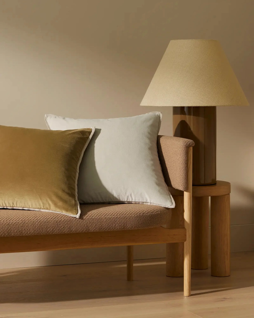 Mid-century modern living room with warm terracotta and cream palette, natural wood sofa and side table, olive and white cushions, linen lampshade, textured upholstery and soft afternoon light