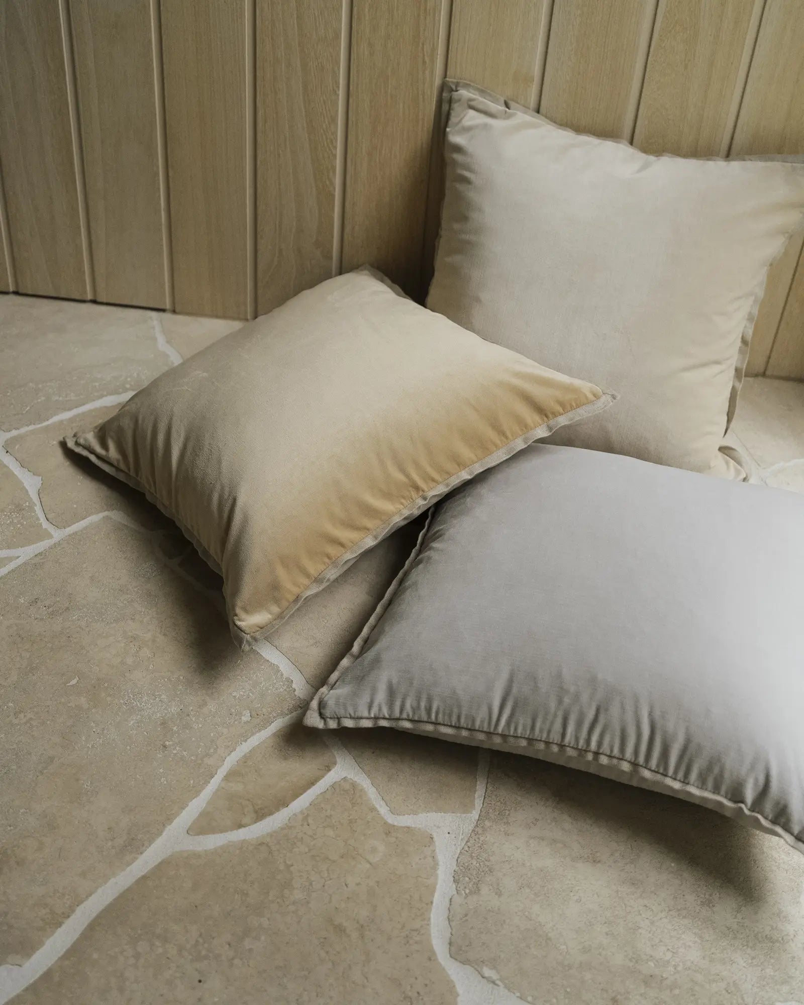 Neutral cushion cluster in cream, beige and soft grey on terrazzo flooring, styled against timber-lined wall for calm, minimalist interior design mood