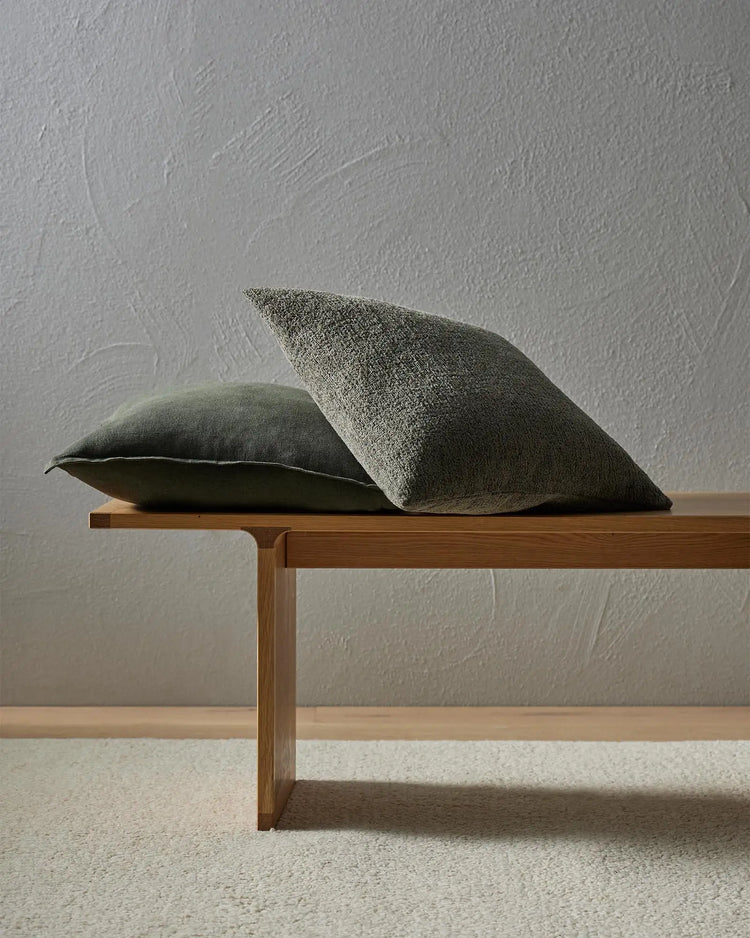 Sage green cushions in textured viscose blend on wooden bench against grey textured wall, minimalist Scandinavian styling with warm timber and neutral tones