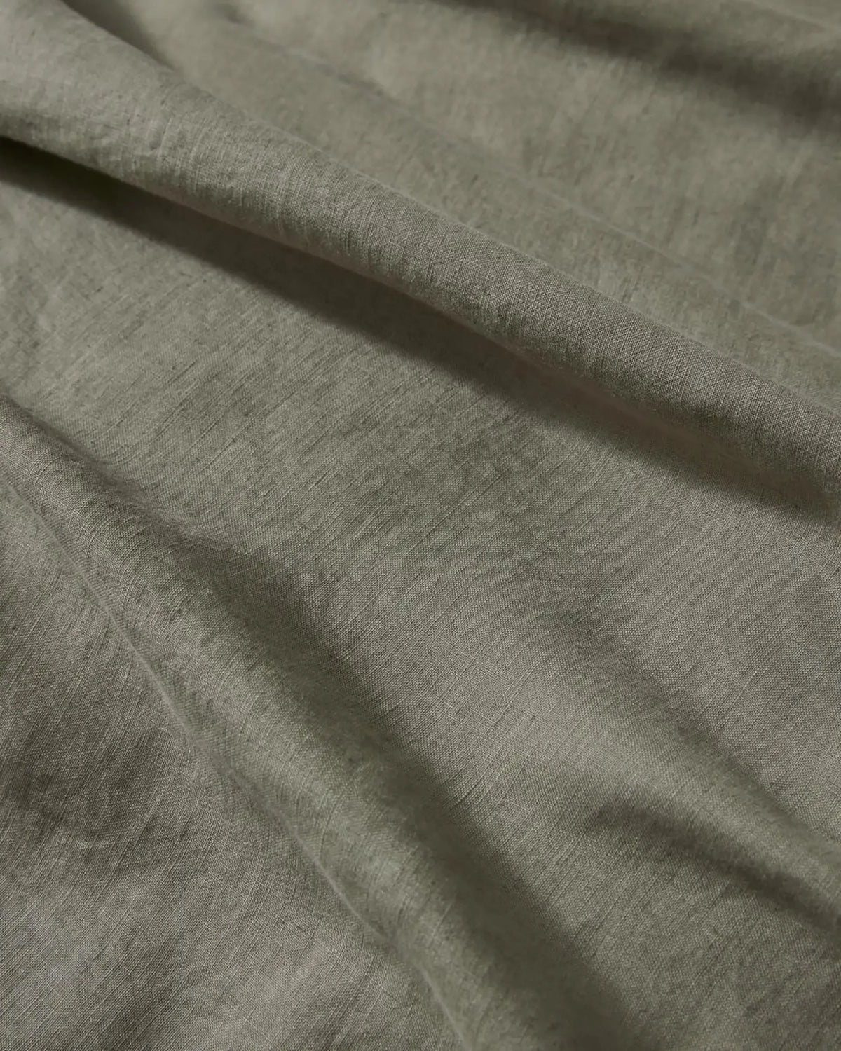 Sage linen bedding detail showing natural texture and soft draping of European linen, capturing warm afternoon light on neutral fabric