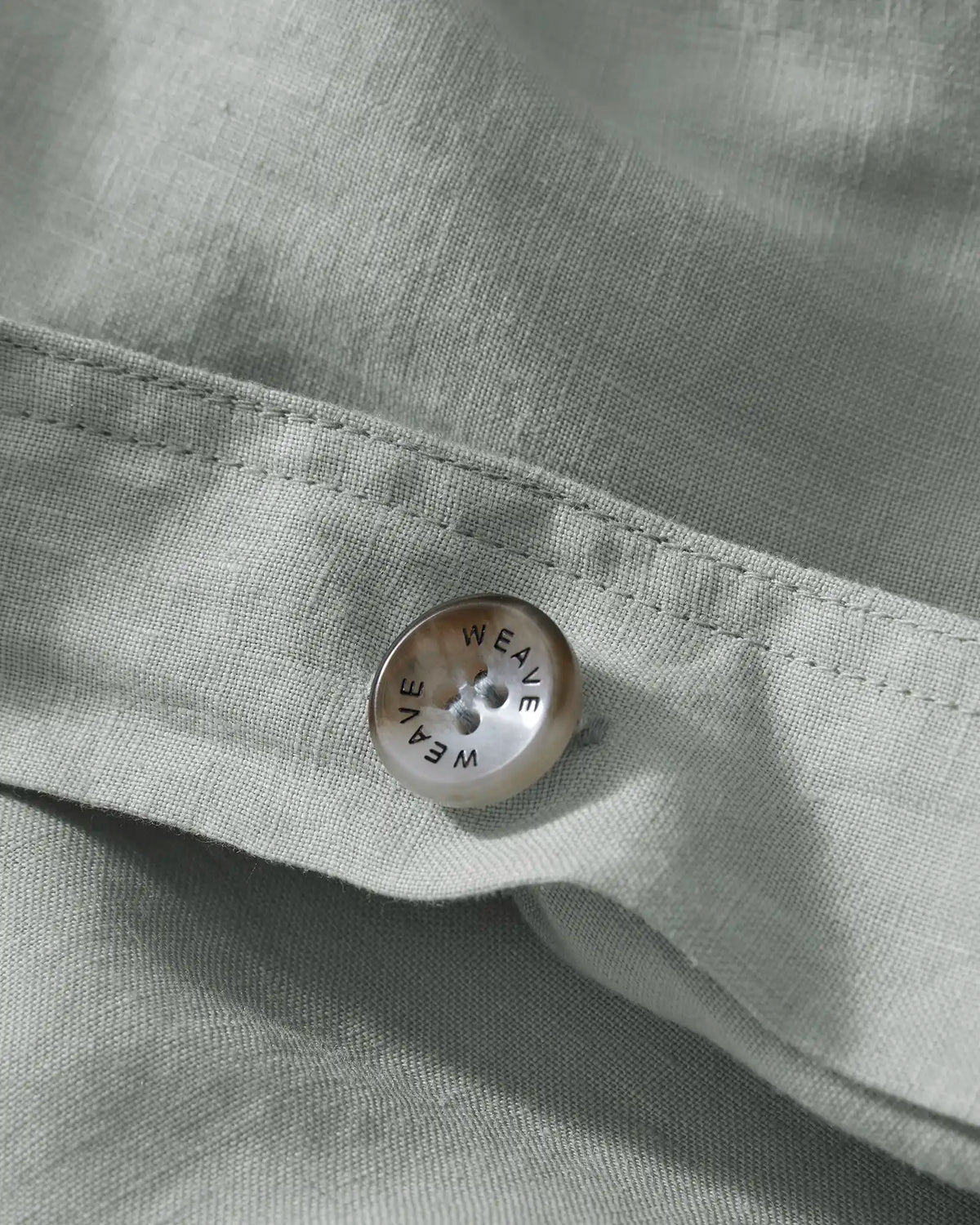 Ravello Quilt Cover button detail in sage, showing branded Weave Home closure button on European linen fabric with blanket stitch seam