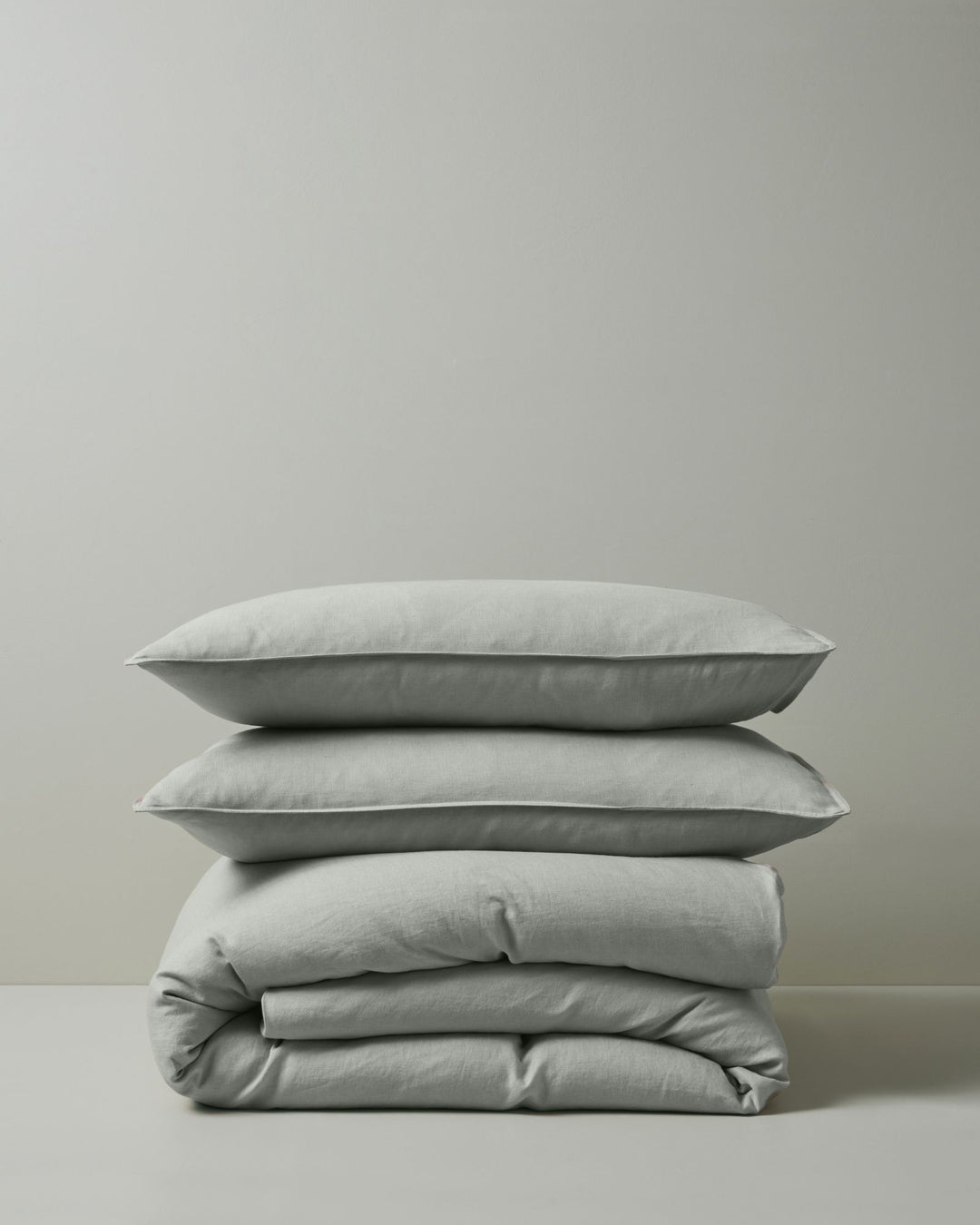 Stacked linen bedding in soft sage tones: Ravello Quilt Cover and Ravello Pillowcase set layered together, showcasing natural texture and neutral minimalist aesthetic