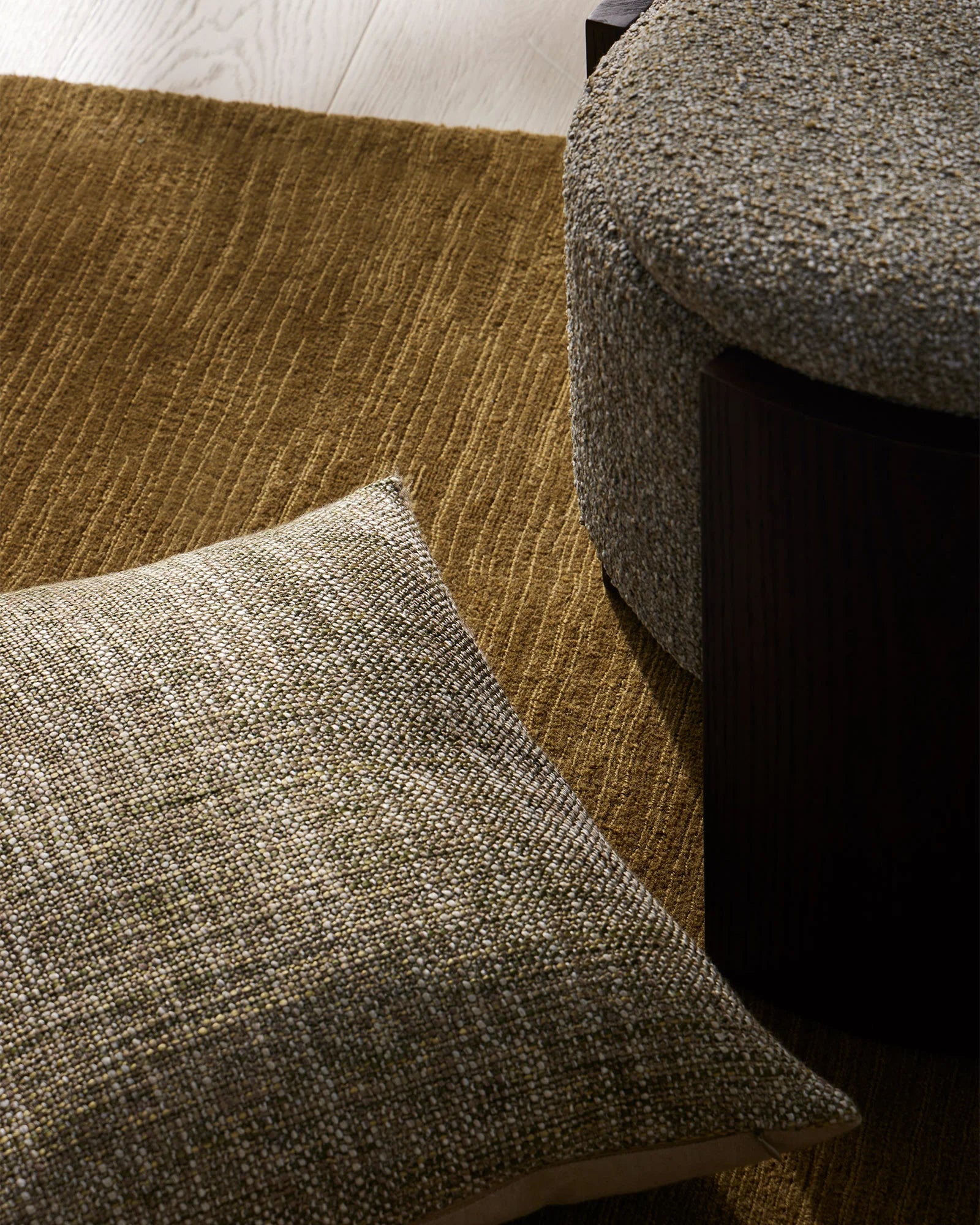 Neutral textured cushion layered on olive-toned upholstered seating, showcasing warm earth-tone palette with woven fabric details and natural lighting