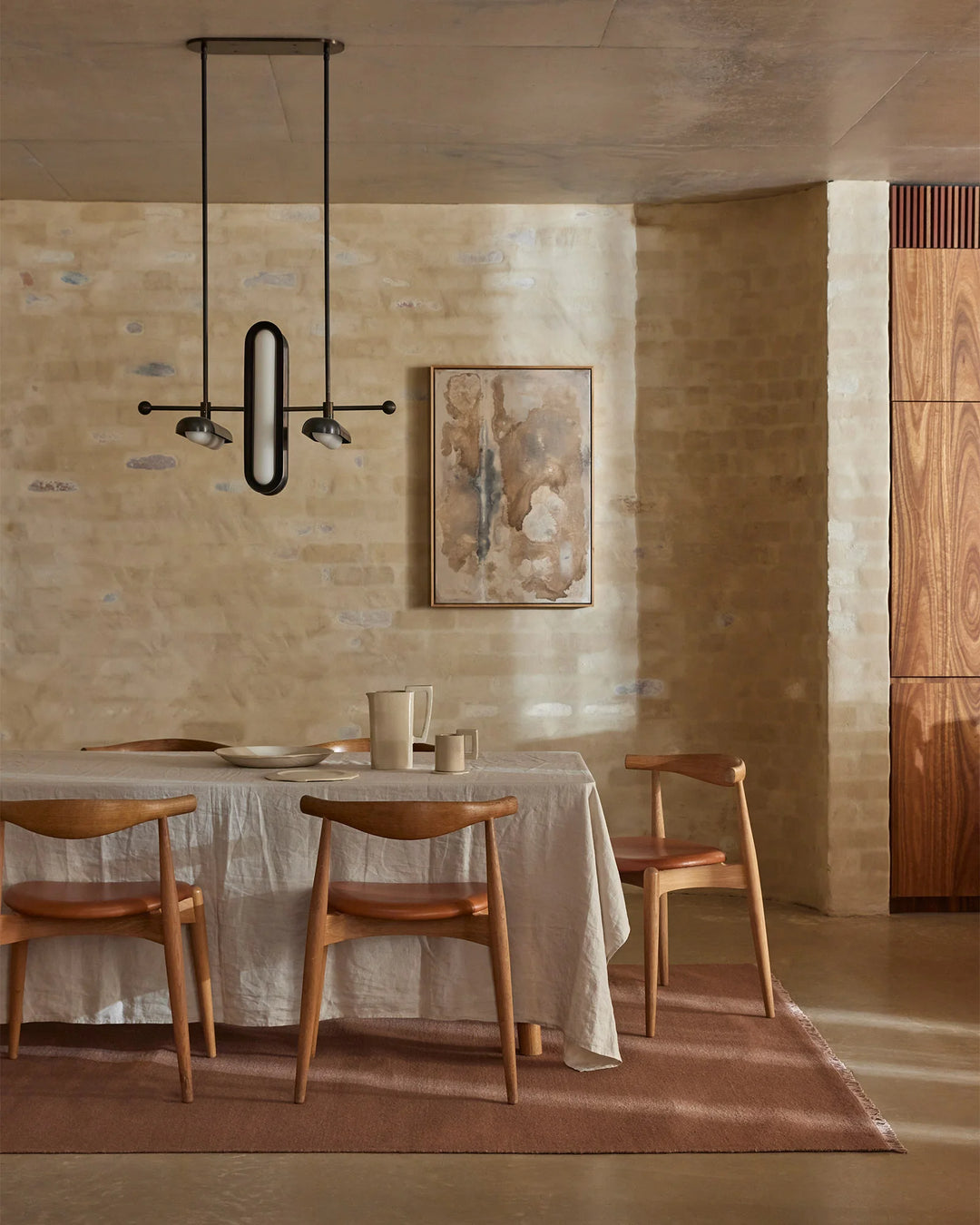 Minimalist dining room with warm terracotta wool rug, natural linen tablecloth, timber chairs, and textured taupe walls in earthy palette