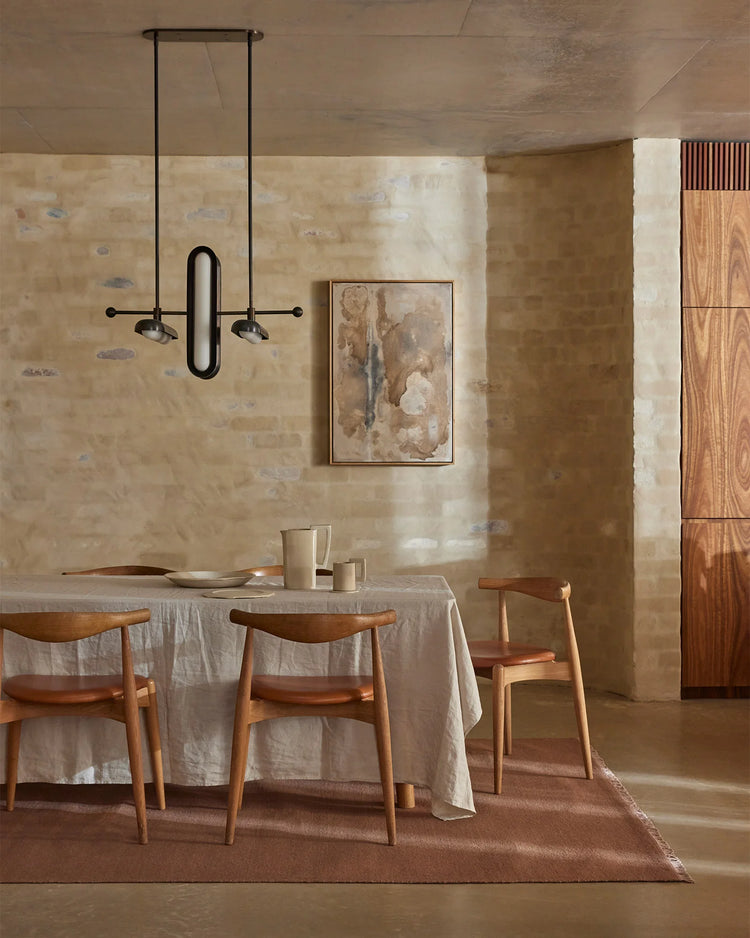 Minimalist dining room with warm terracotta wool rug, natural linen tablecloth, timber chairs, and textured taupe walls in earthy palette