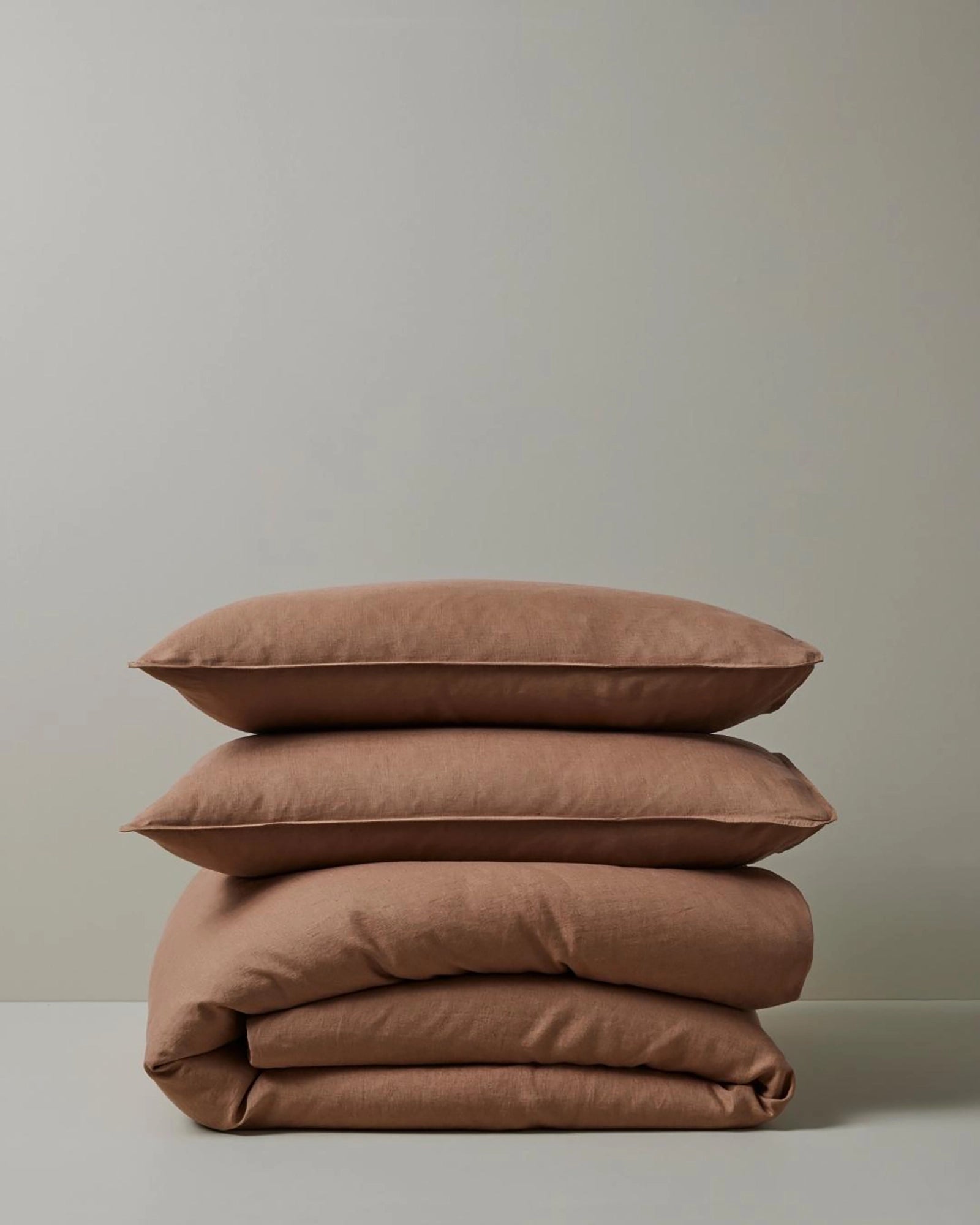 Stacked Ravello Quilt Cover and Pillowcase Set in biscuit, showcasing warm terracotta and neutral tones with soft linen texture and minimalist styling