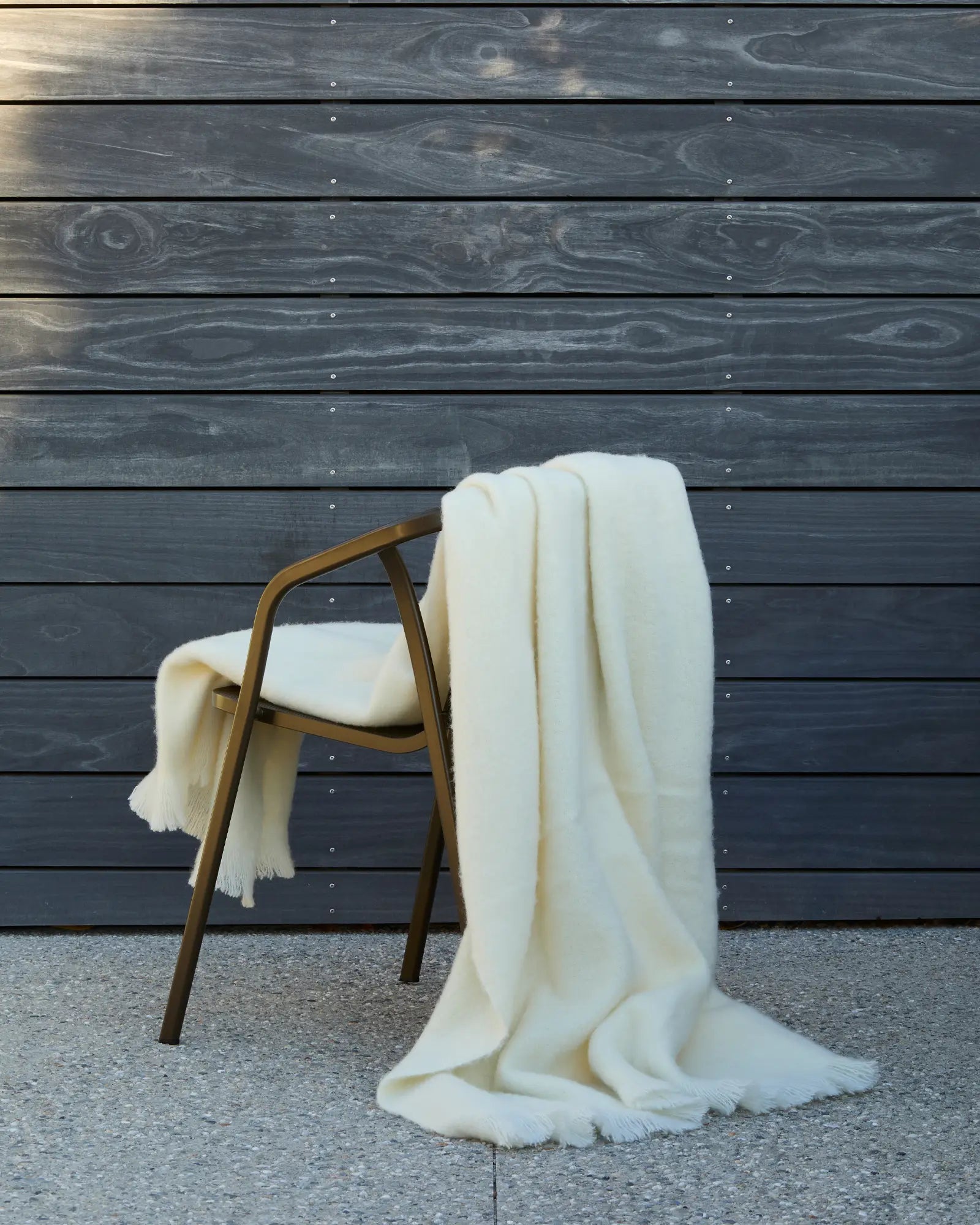 Hyde Cream wool blend throw with fringe trim draped over timber chair, soft vanilla-toned woven texture by Weave Home