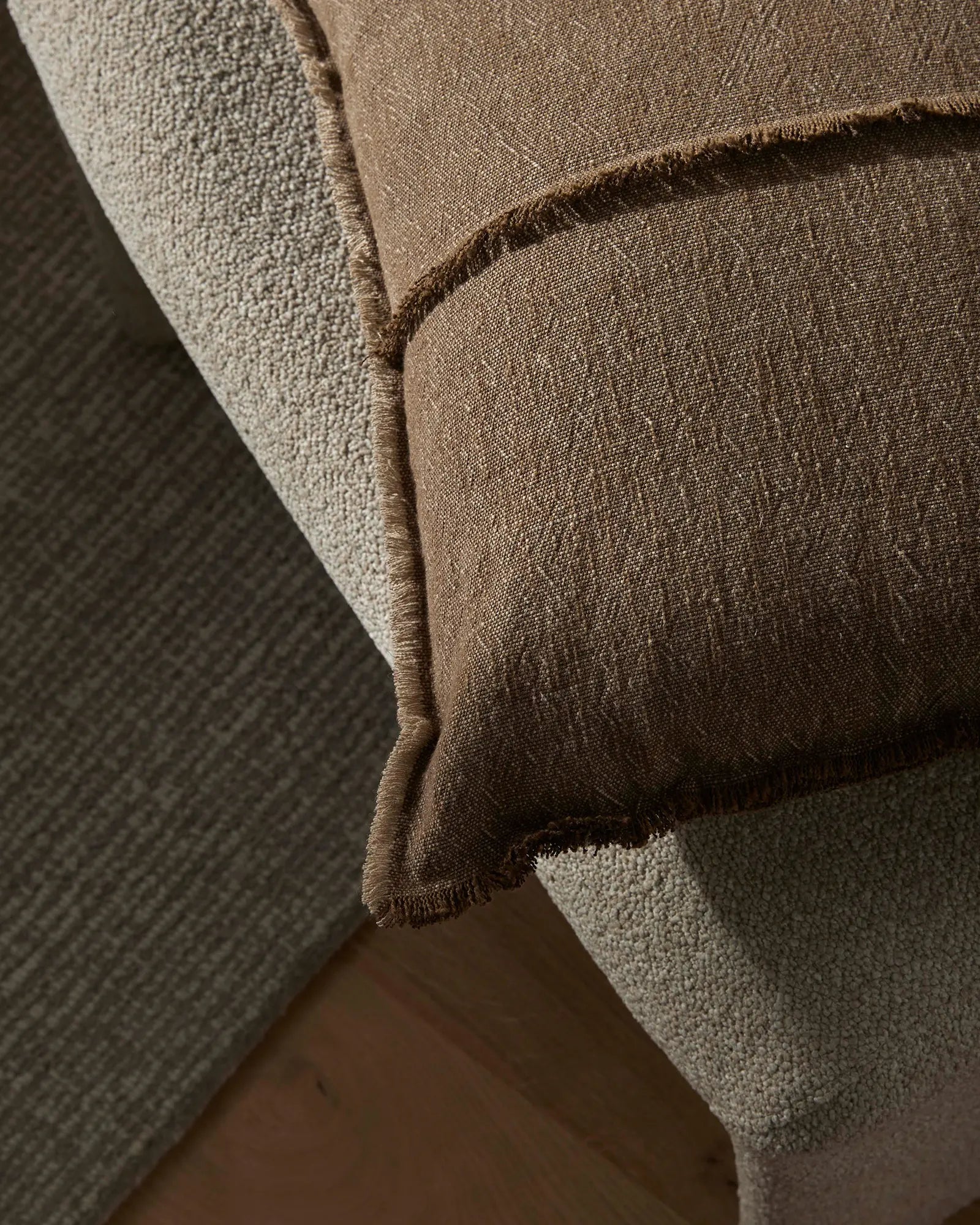 Neutral linen cushion with raw-edge framing draped over cream boucle upholstery, highlighting natural textile textures and warm earth-tone palette