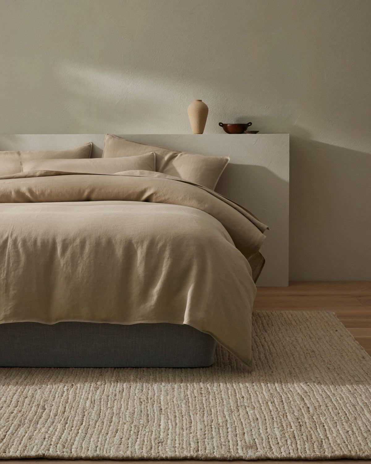 Minimalist bedroom with neutral linen bedding, textured jute rug, and earthy pottery styling, warm beige palette and calm aesthetic