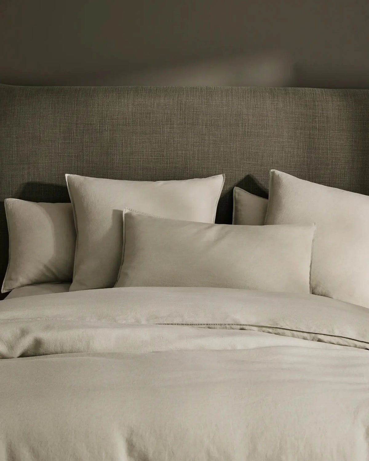 Neutral linen bedding styled on a sage upholstered bed with layered cream pillows and Ravello Fitted Sheet in soft, textured European linen