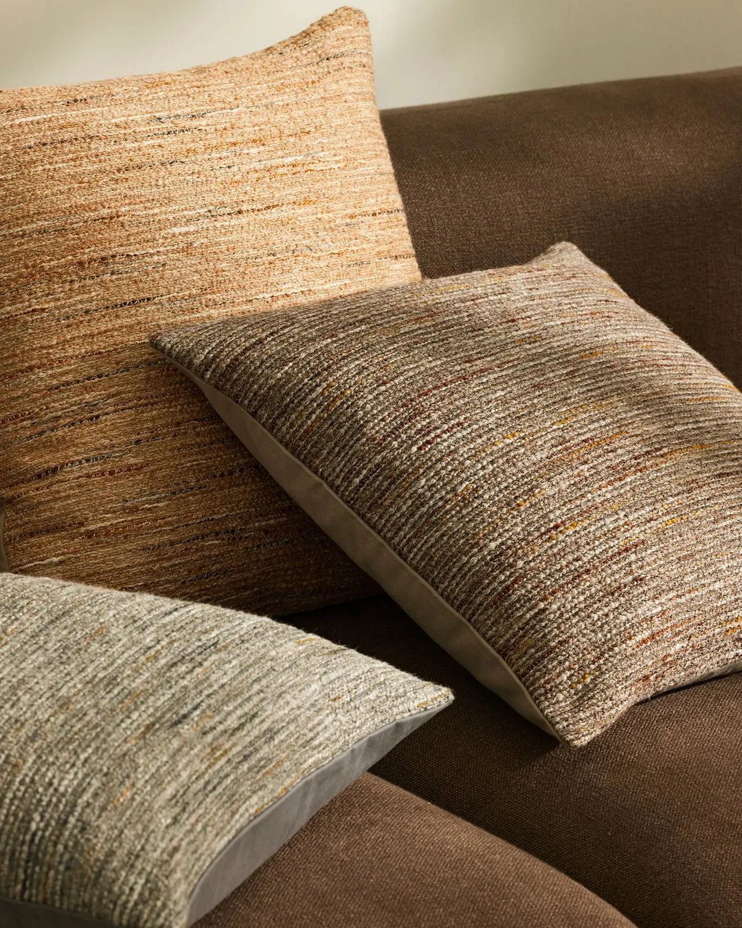Neutral earthy cushions in sage, natural and warm tones layered on a charcoal sofa, showcasing textured woven fabrics and organic palette styling