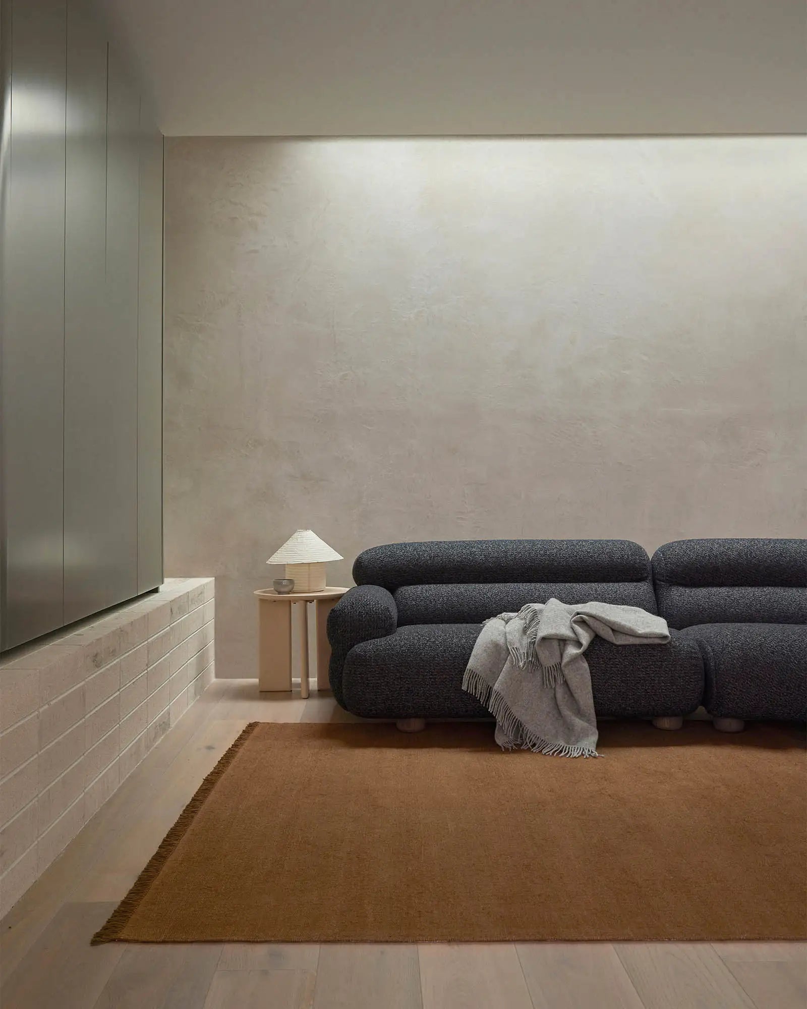 Minimalist living room with charcoal sofa, toffee linen rug, soft grey throw, and warm neutral palette creating serene contemporary interior styling