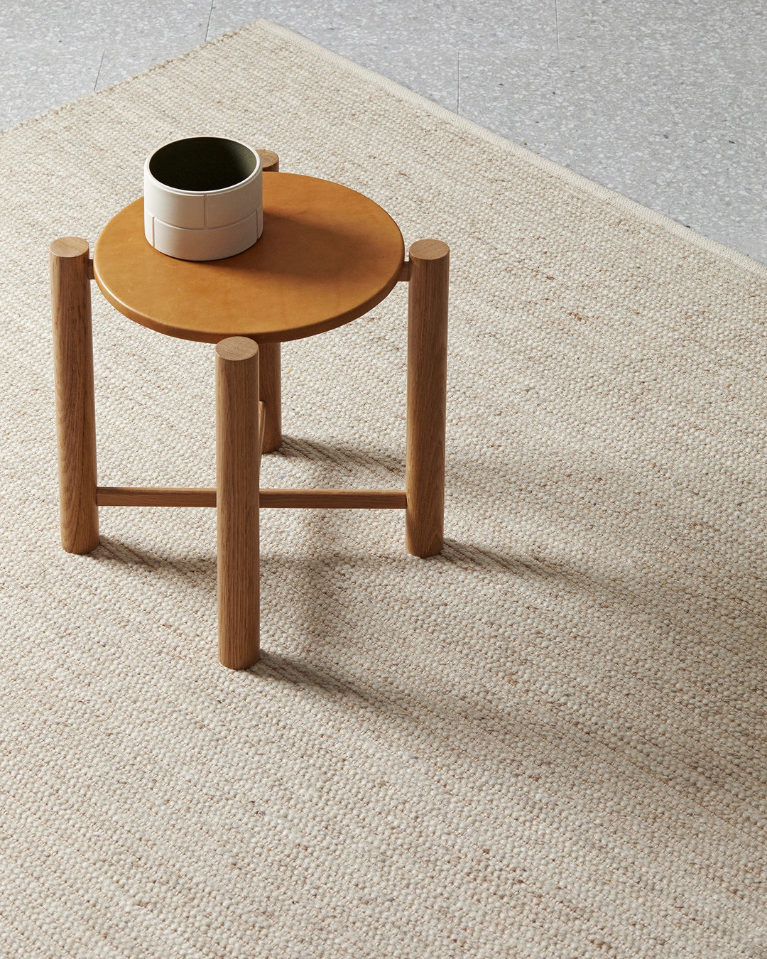 Neutral wool-cotton blend rug in warm sand tone grounds a minimalist wooden side table with ceramic mug in Scandinavian-inspired interior styling