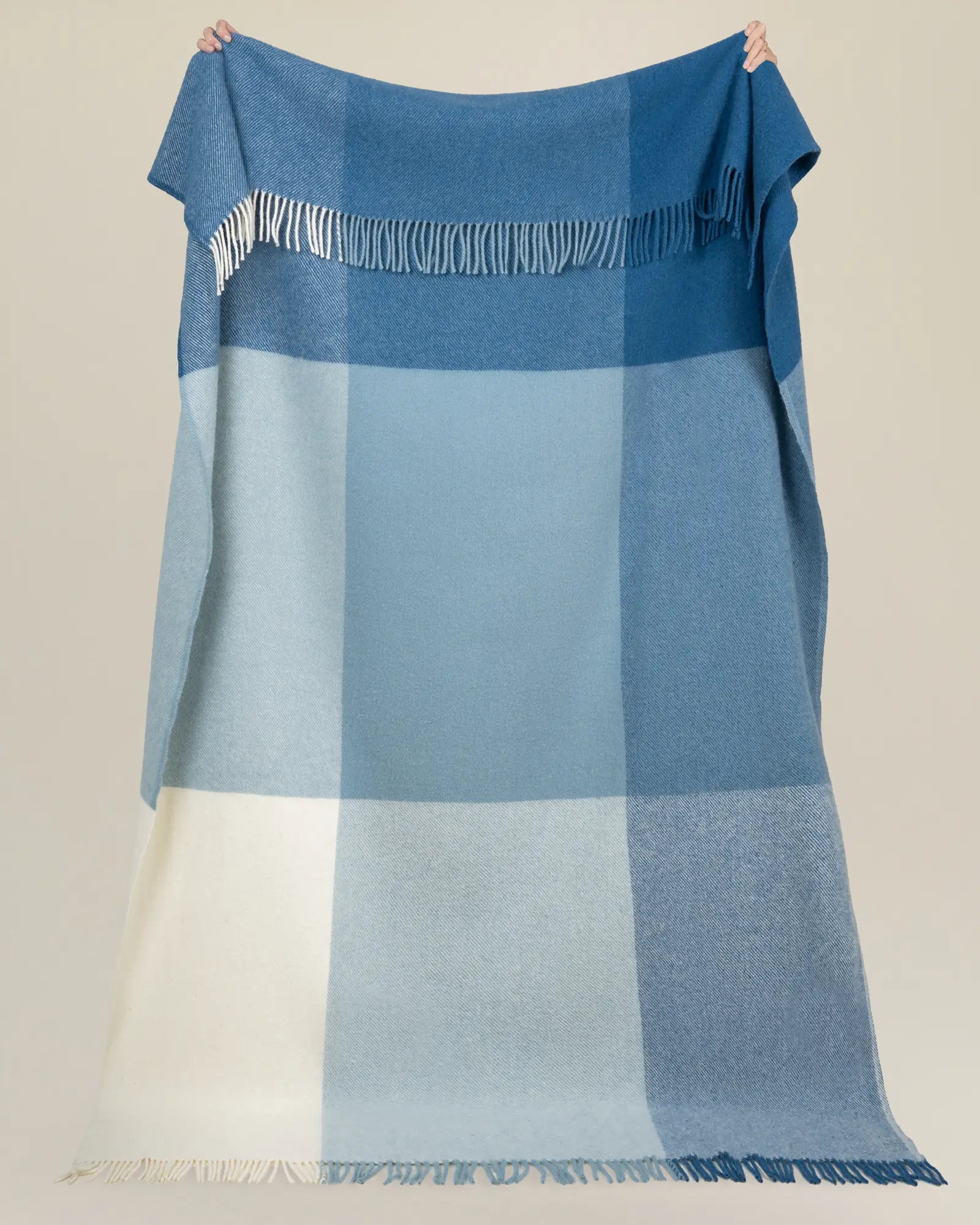 Bayswater Breeze wool throw in blue and white check with fringe border, held up to show colour blocking and soft NZ wool texture by Weave Home