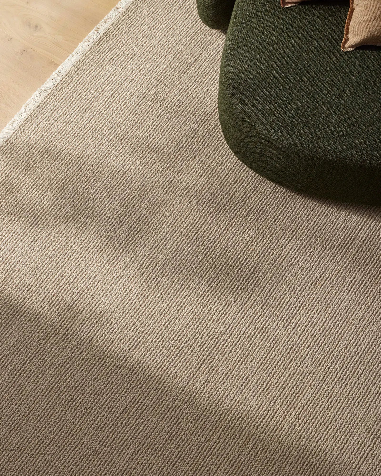 Neutral wool rug with fine linear texture anchoring a living space, styled with olive green upholstered seating and warm wood flooring for a contemporary, earthy aesthetic.
