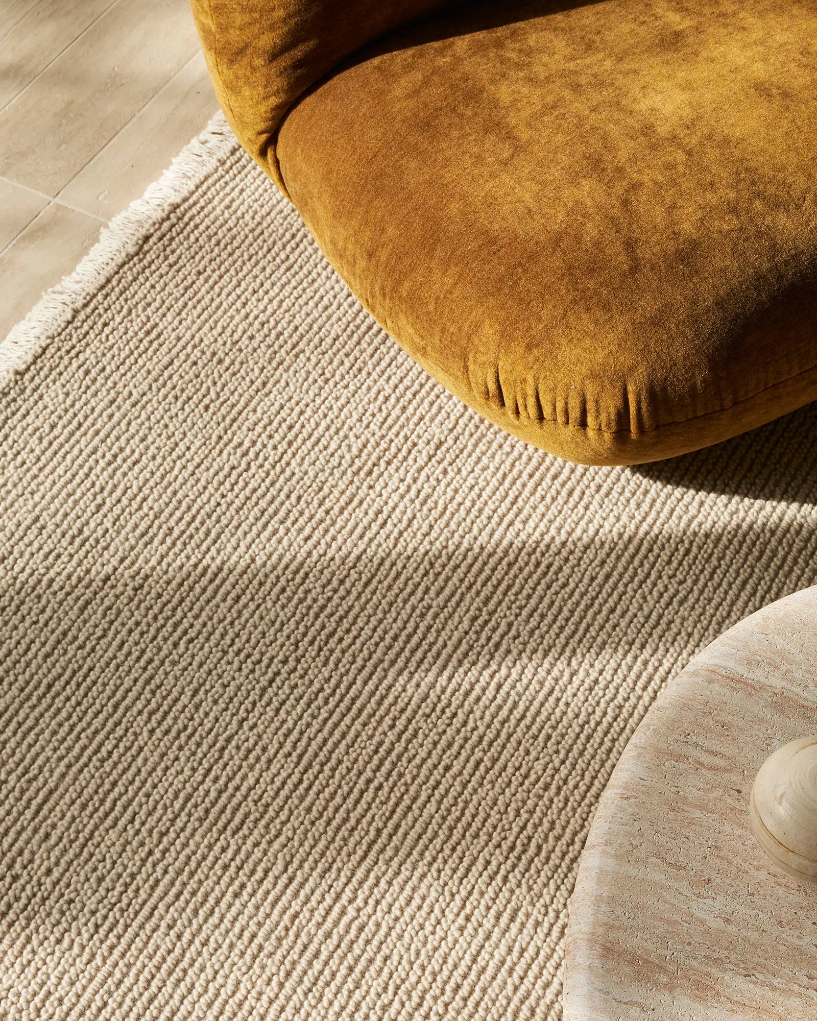 Ochre wool chair with fringed edge sits on neutral Fabien stone wool rug, warm earthy palette against pale timber flooring