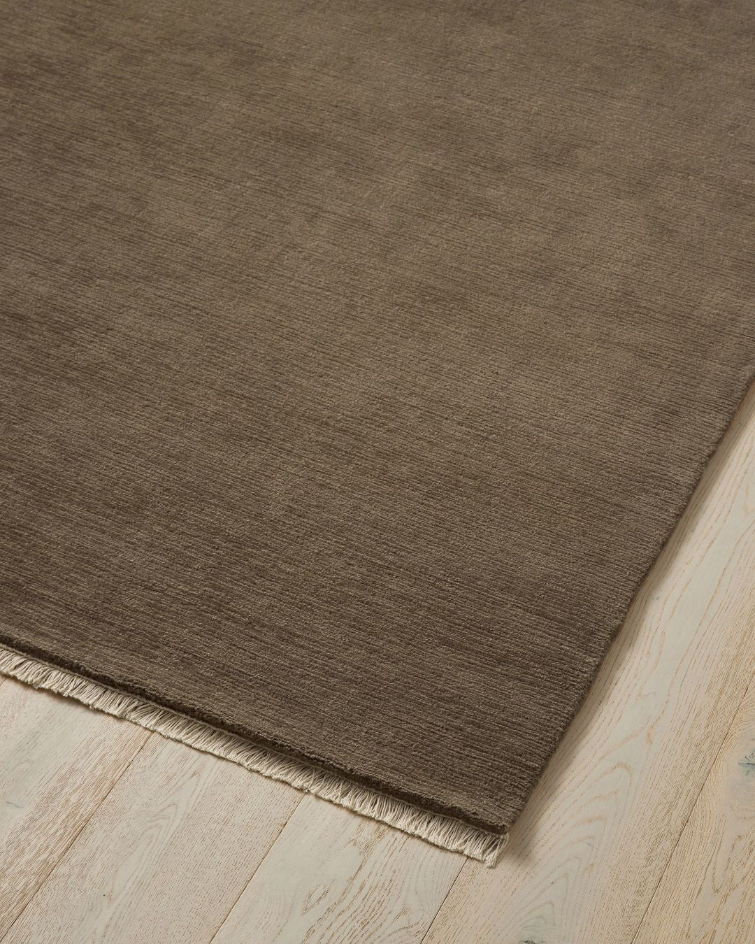 Alessandre Taupe hand-woven wool rug with fringe edge detail on light wood floor by Weave Home