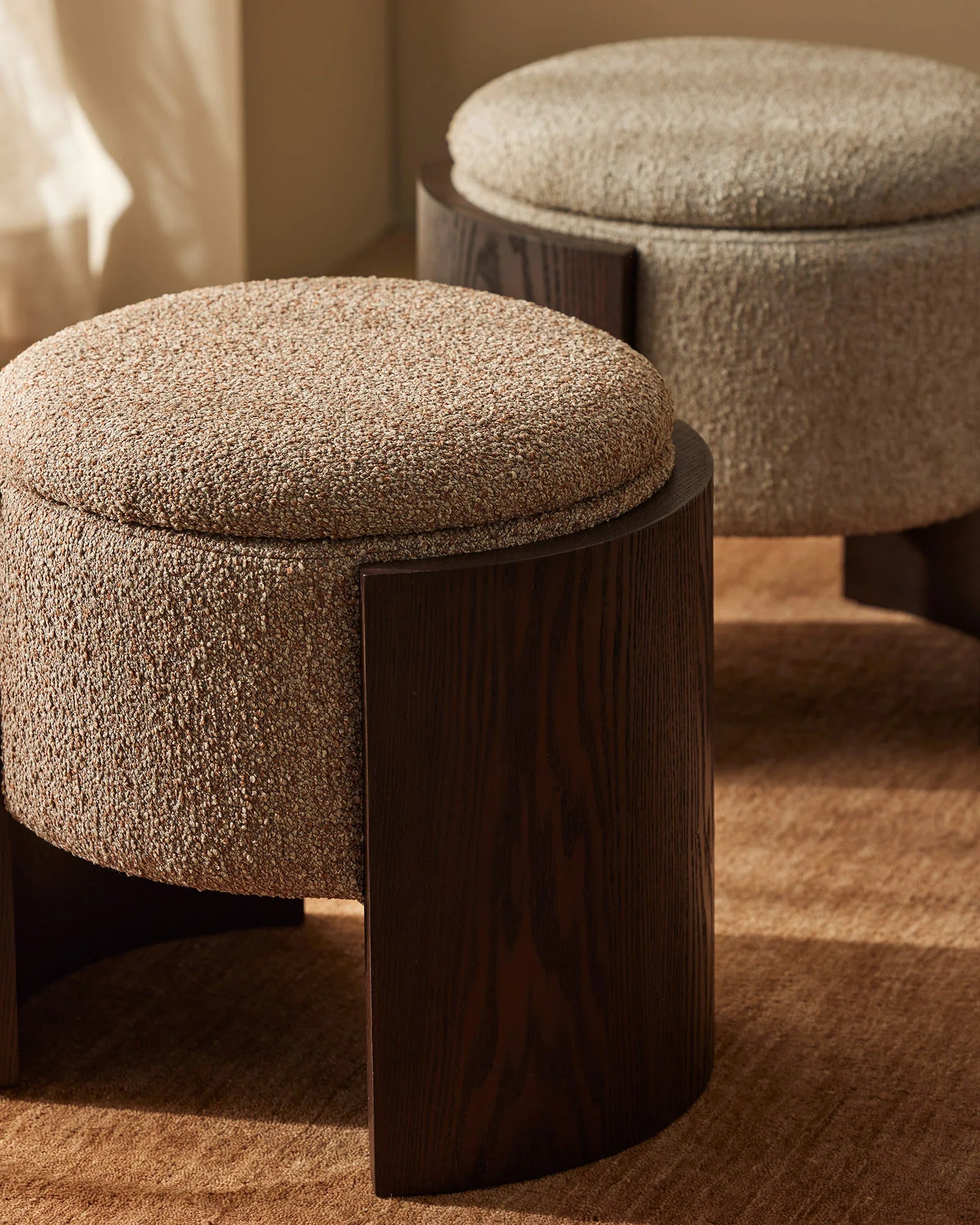 Warm neutral living space with Norcia ottomans in textured cream and stone fabrics, dark wood bases, and woven rug on warm toned walls