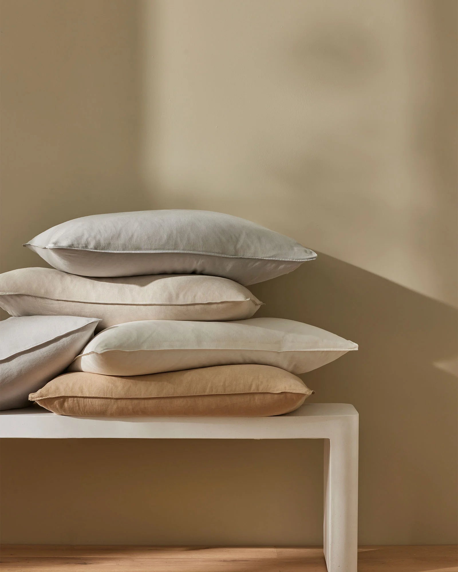 Stacked Ravello Pillowcase Set in neutral linen tones, displaying cream, ivory and warm sand hues against soft taupe wall and wooden floor