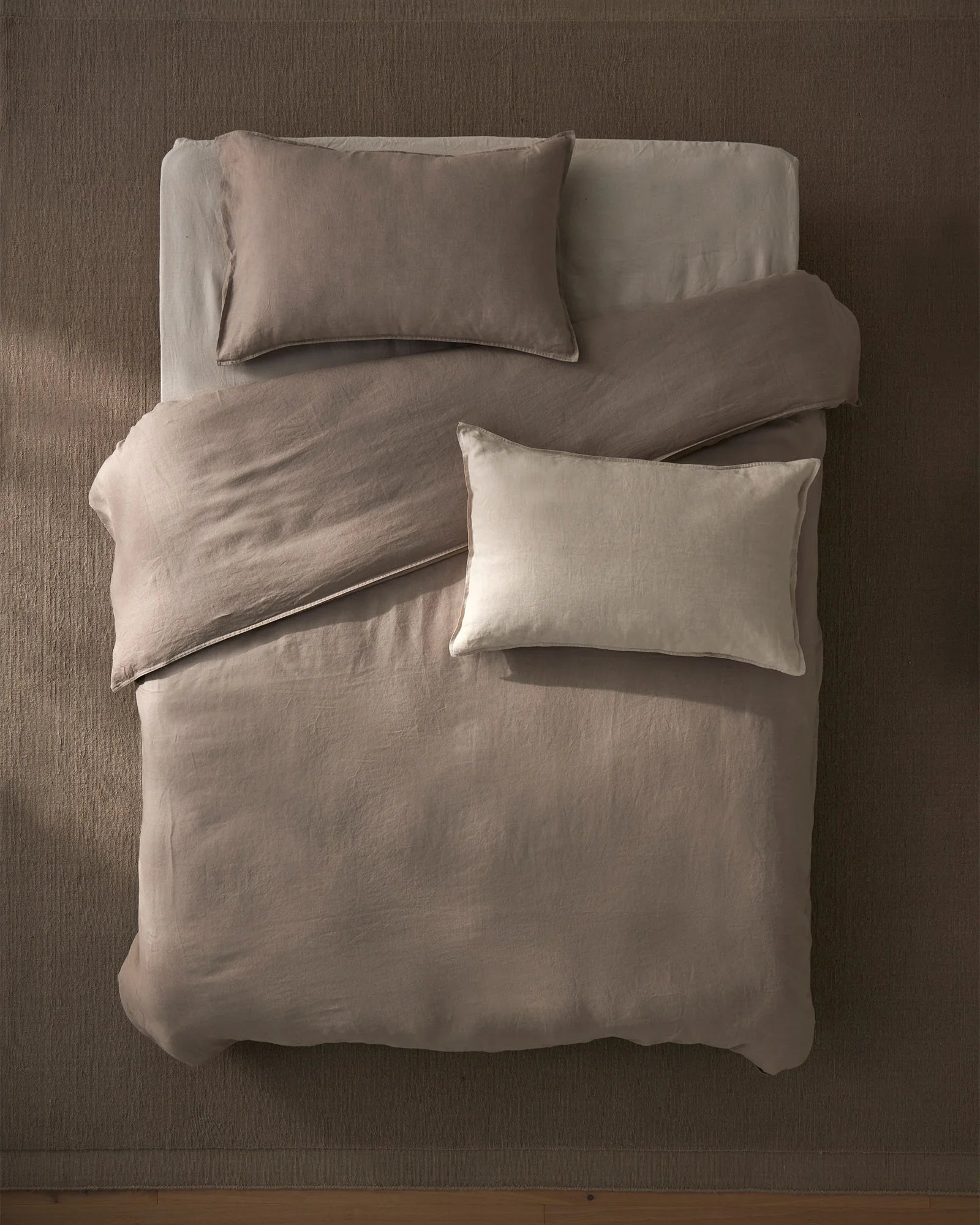 Overhead view of bed styled with neutral linen bedding in warm taupe and cream tones, Ravello Quilt Cover and Fiore cushions creating a serene, minimalist bedroom aesthetic with soft linen textures