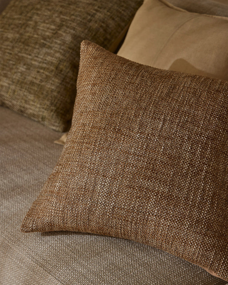 Warm neutral cushions in taupe and toffee tones layered on a cream upholstered sofa, showcasing textured woven fabrics and earthy minimalist interior styling
