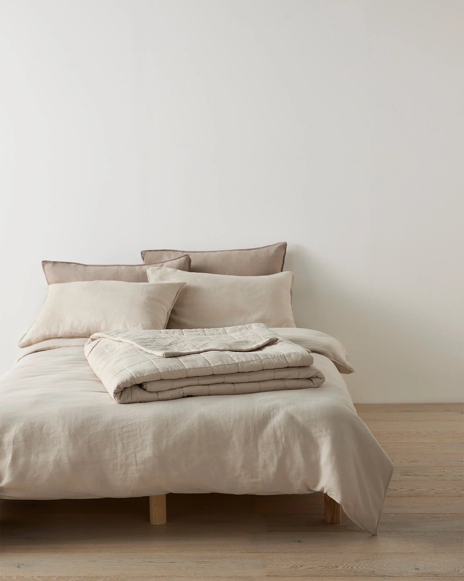 Neutral bedroom styling with layered linen bedding in cream and taupe tones, Ravello coverlet folded across natural wood bed frame, soft textured fabrics and minimalist aesthetic