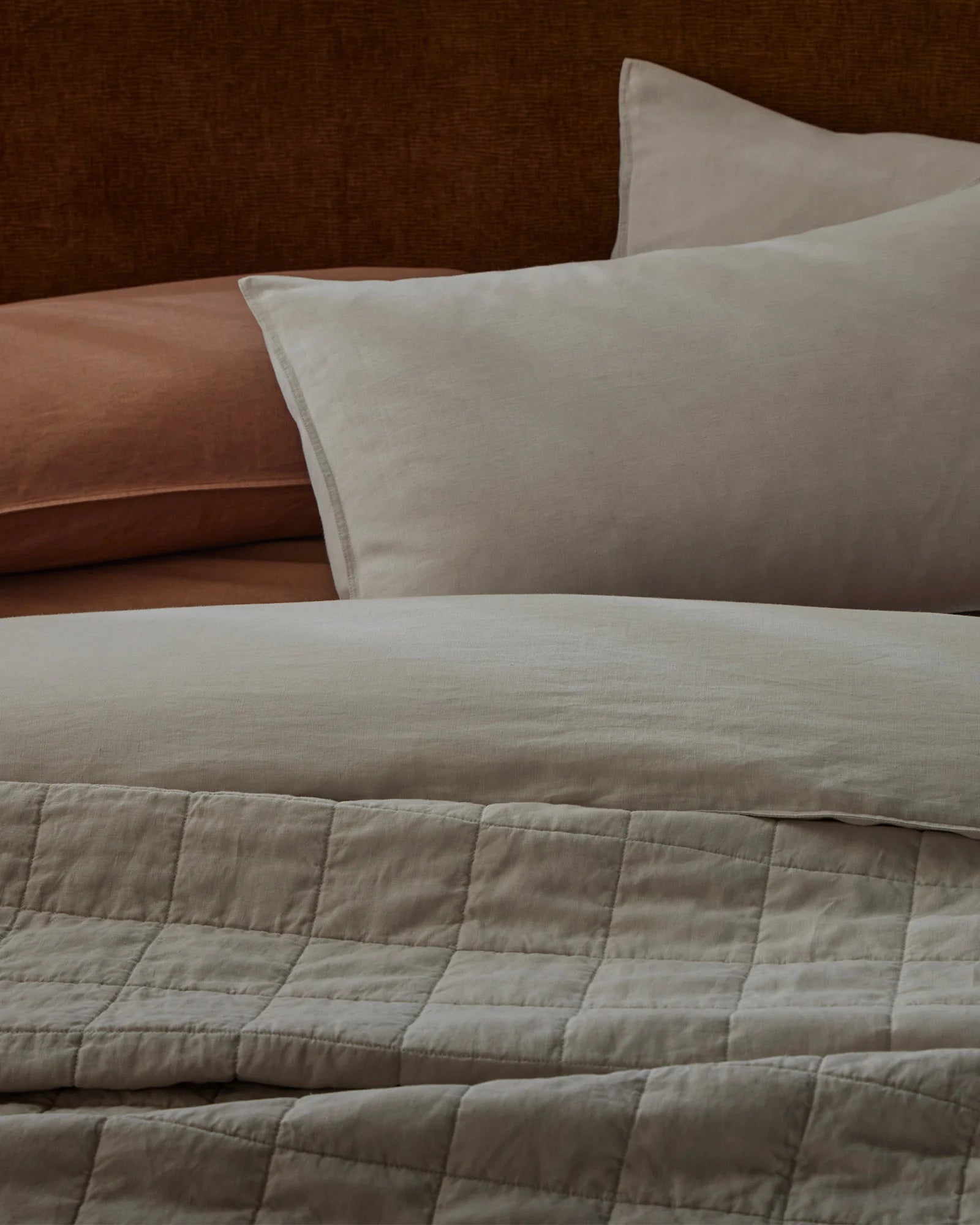 Warm-toned bedroom styled with cream linen pillows and quilted Ravello coverlet layered over terracotta and chocolate bedding for earthy, textured appeal