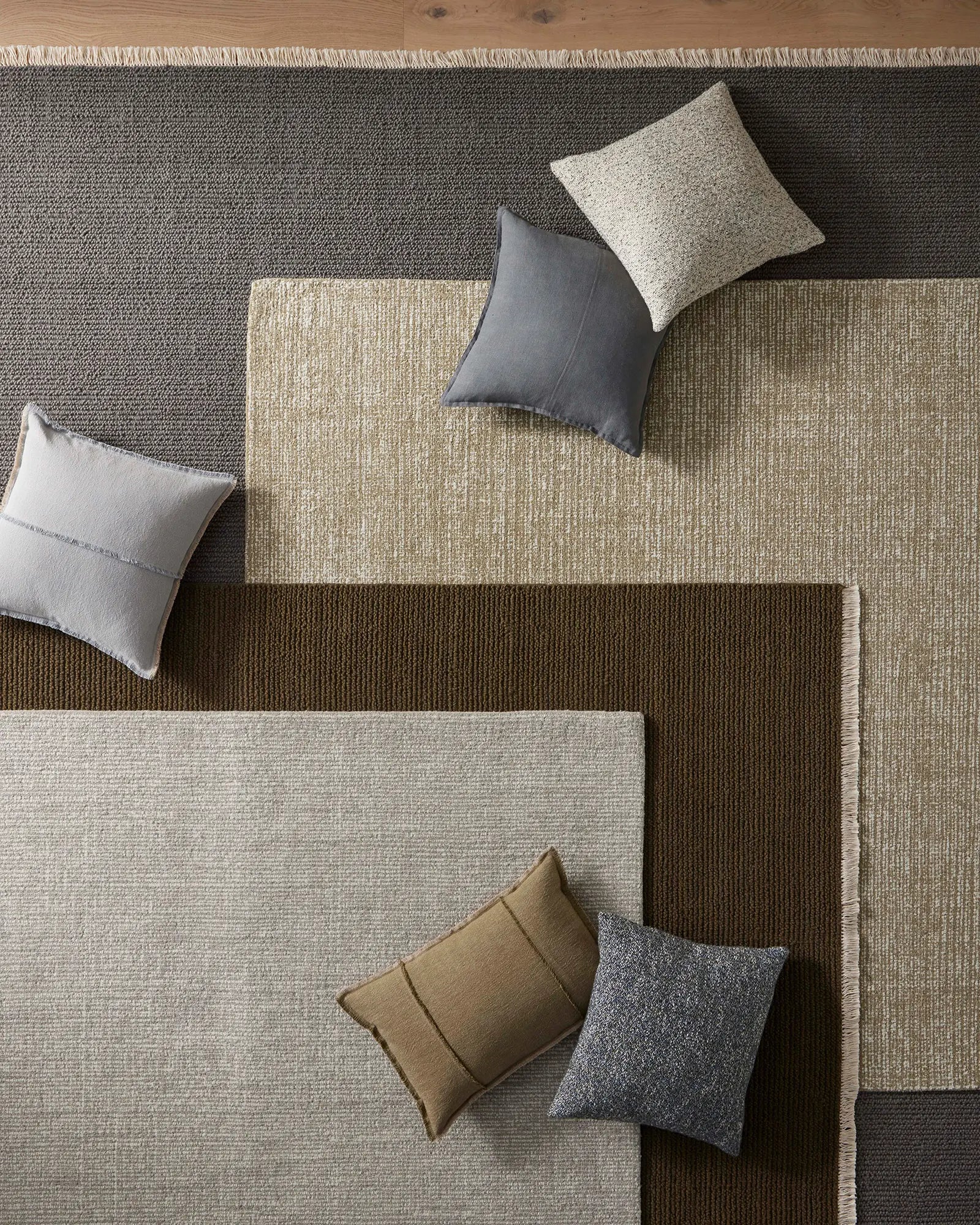 Overhead view of earth-toned interior with layered textured rugs in charcoal, sage and chocolate, styled with Como Steel linen cushions and coordinating pillows in neutral and slate tones