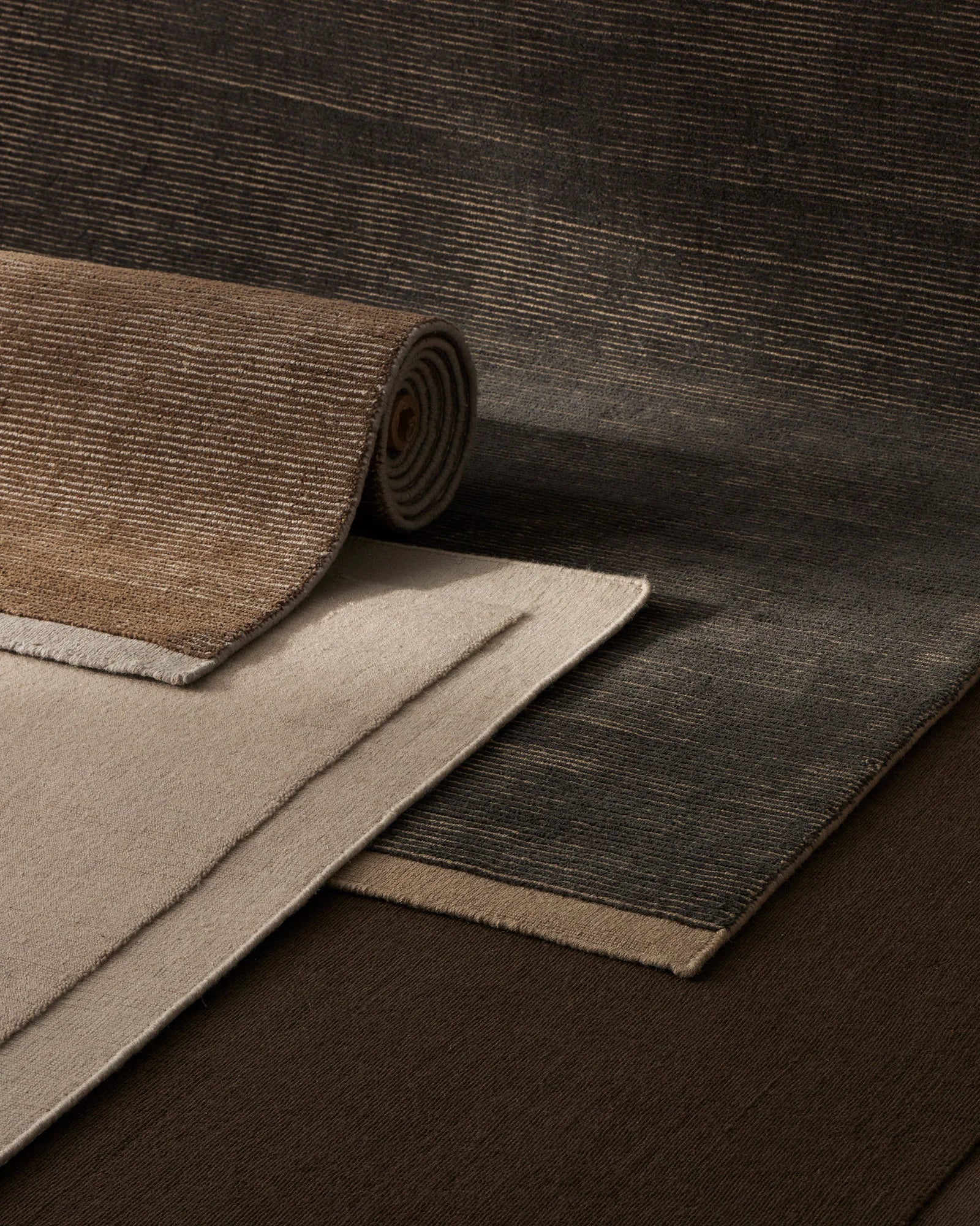 Layered wool rugs in charcoal, taupe and sand tones showcase textured ribbed weave and natural fibre depth in neutral interior styling