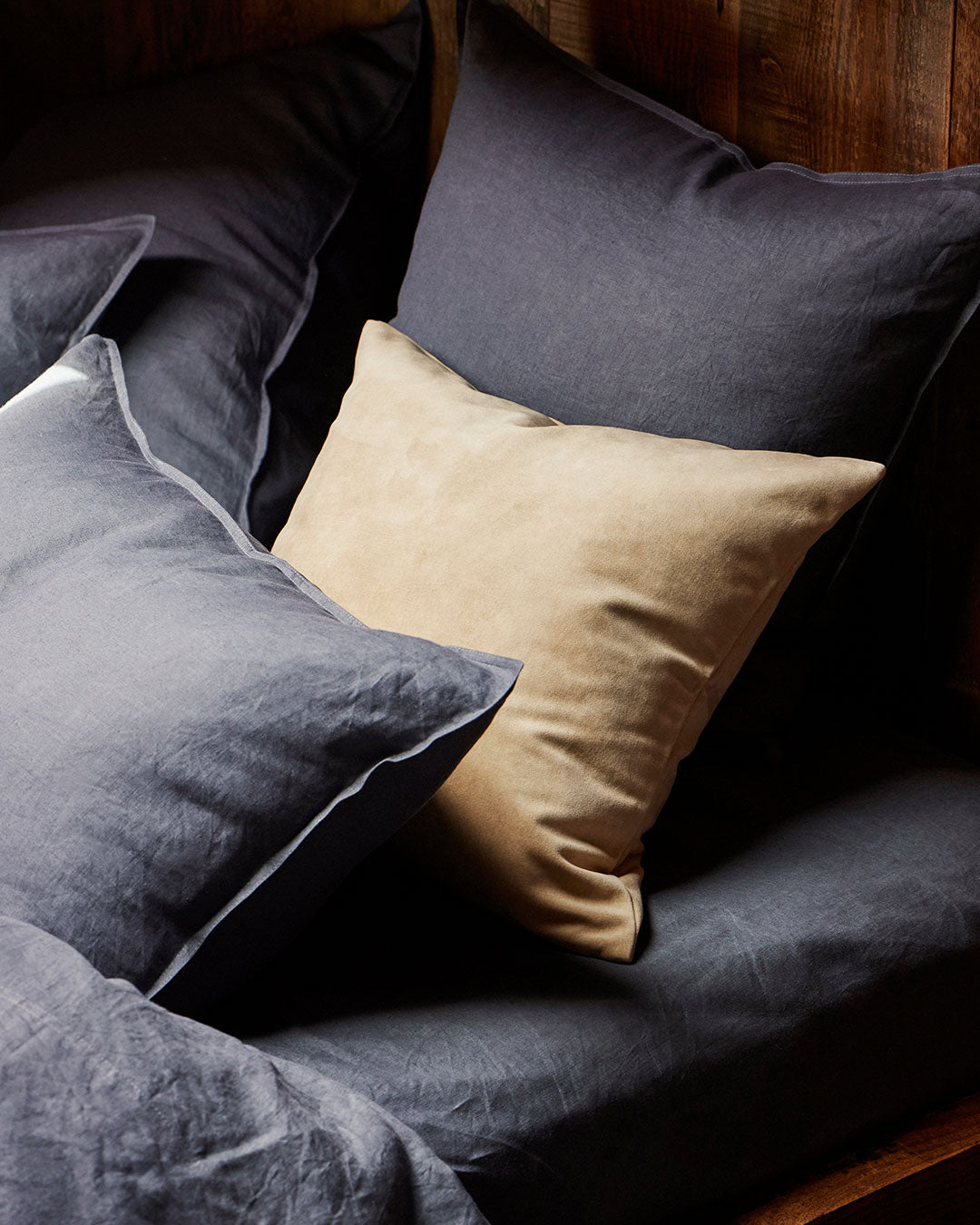 Ravello flat sheet in denim paired with natural linen cushion, showing contrast piping detail and relaxed European linen texture by Weave Home