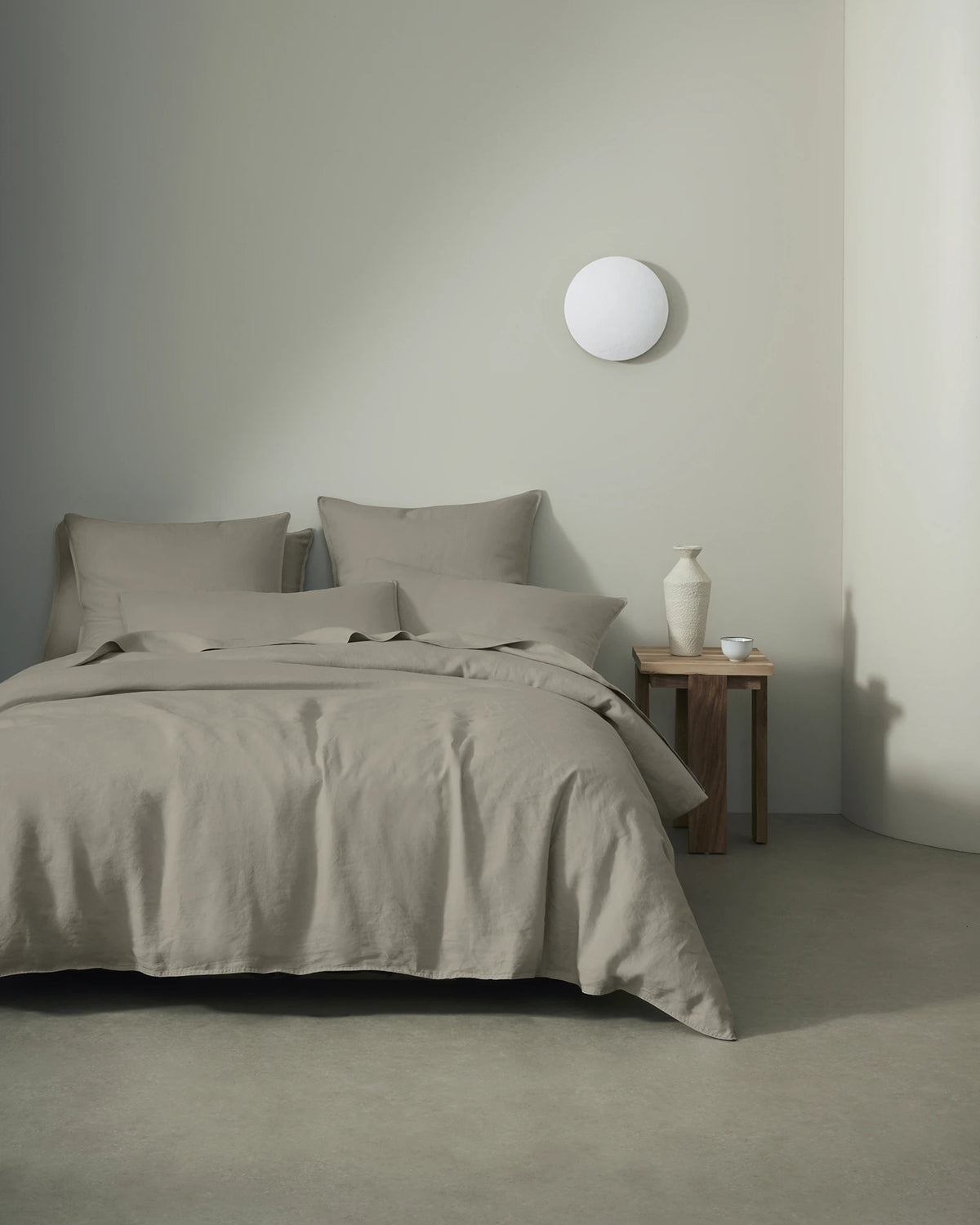 Minimalist bedroom with Ravello linen bedding in pebble grey, featuring soft linen texture and natural draping against neutral walls and warm wood nightstand