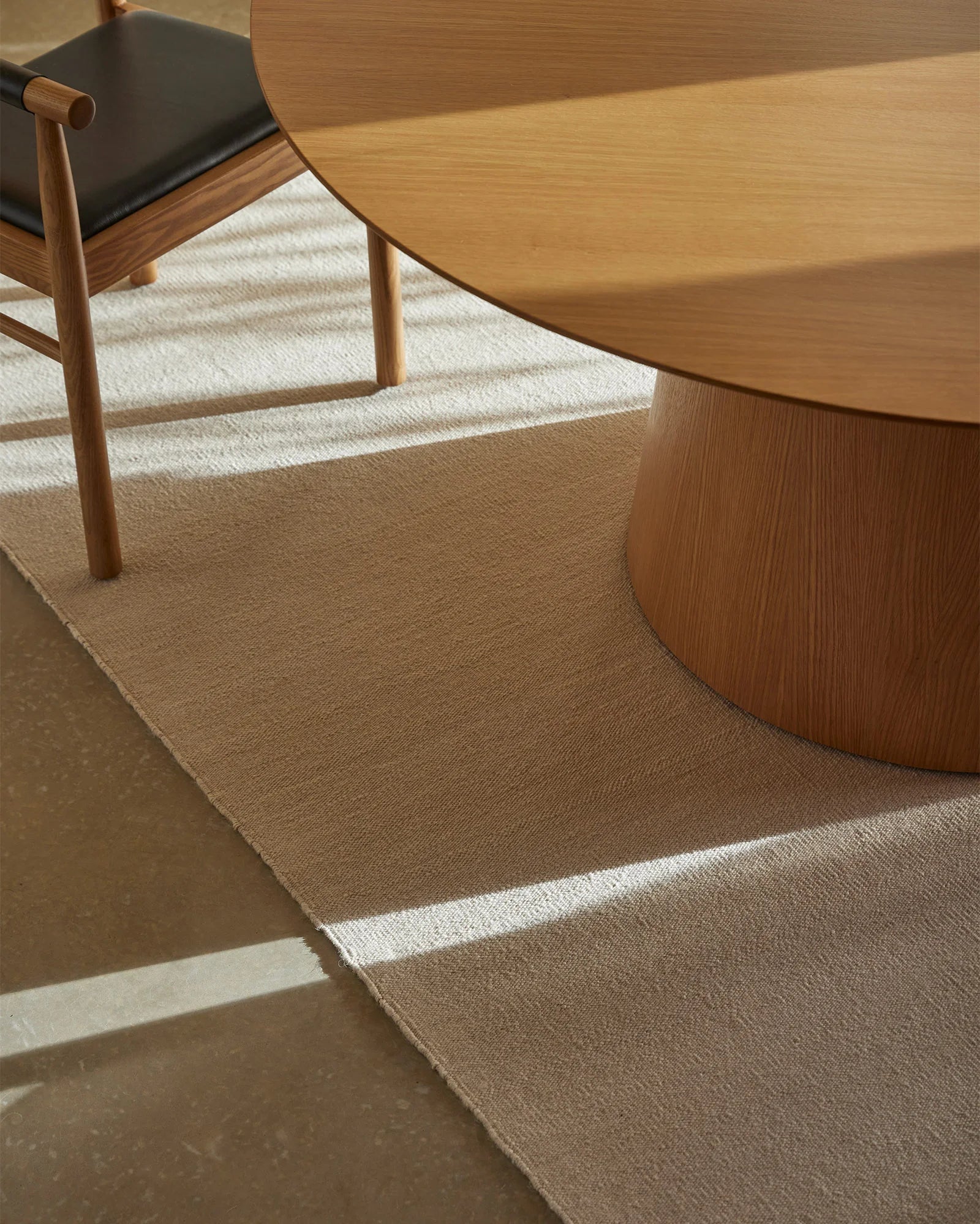 Warm minimalist workspace with natural wood furniture and layered neutral rugs in cream and taupe, showcasing textured wool flooring and mid-century modern styling