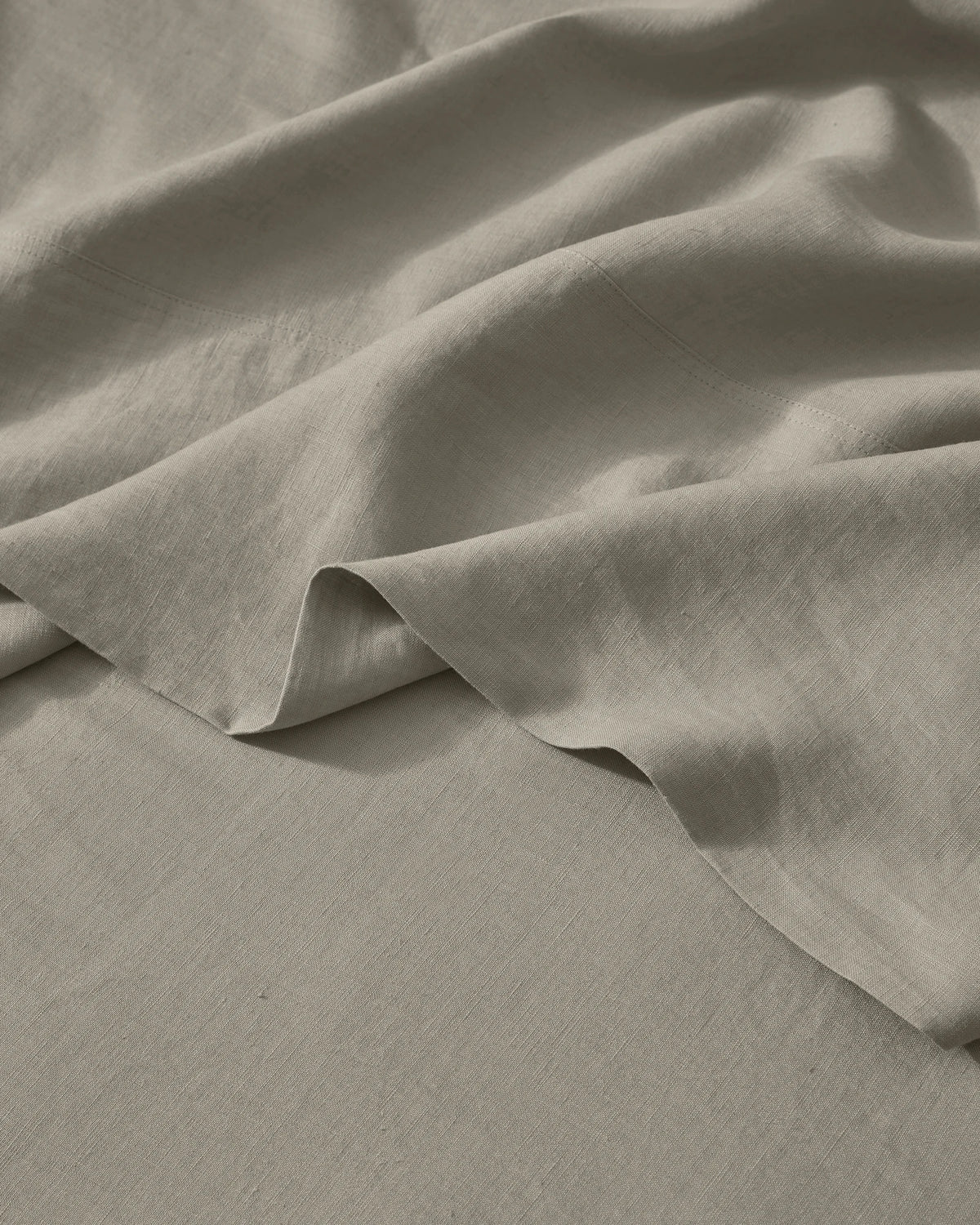 Close-up of soft pebble linen bedding with natural texture and folds, showing lightweight European linen weave in neutral warm tones