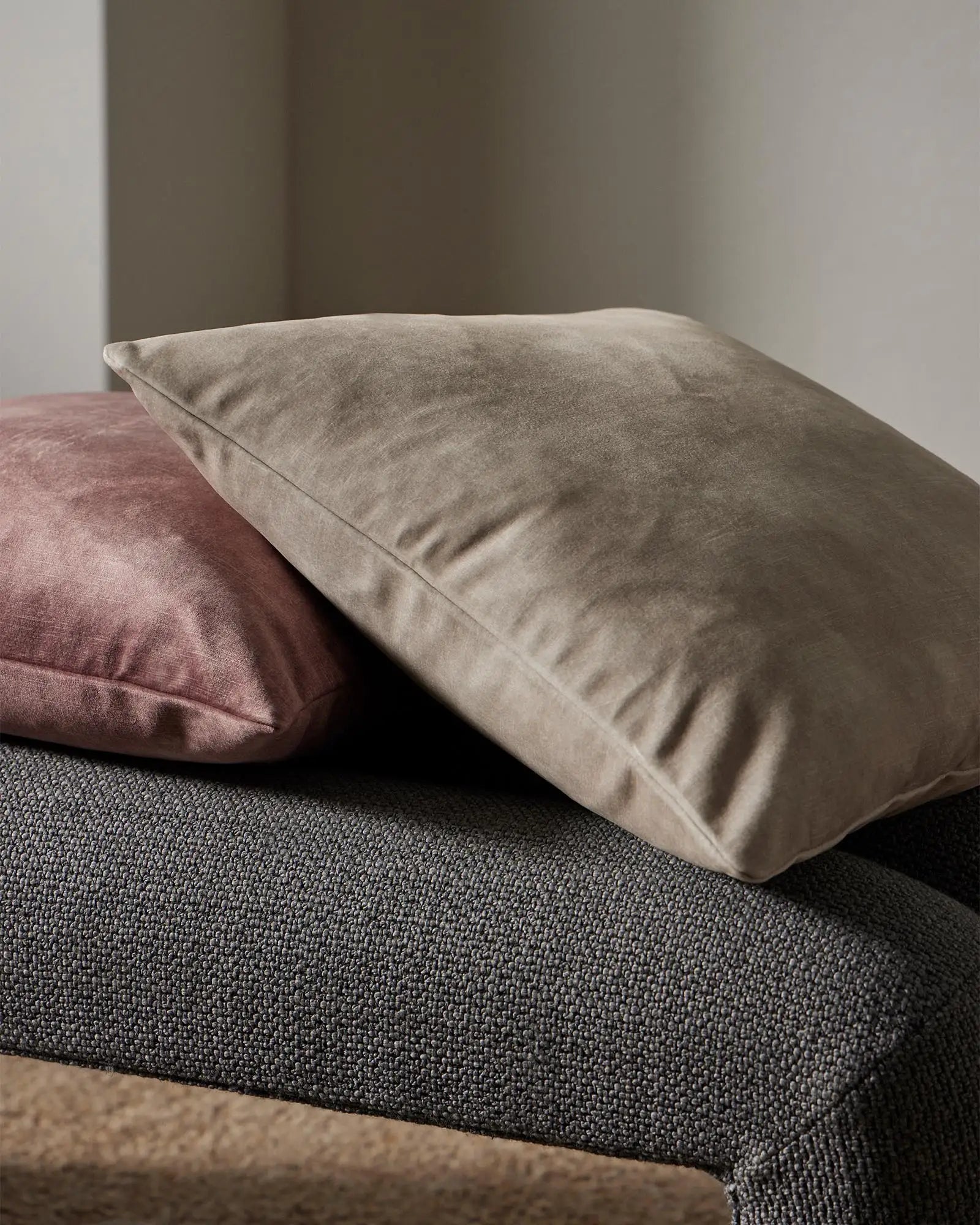 Neutral and mauve cushions layered on charcoal upholstered seating, showcasing soft polyester textures and an earthy, minimalist interior styling palette