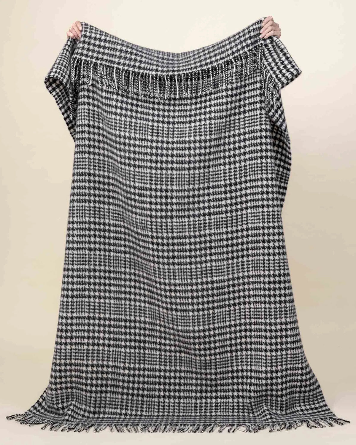 Helmsdale Midnight wool throw in classic black and white houndstooth check with hand-tied fringe border, held aloft by Weave Home