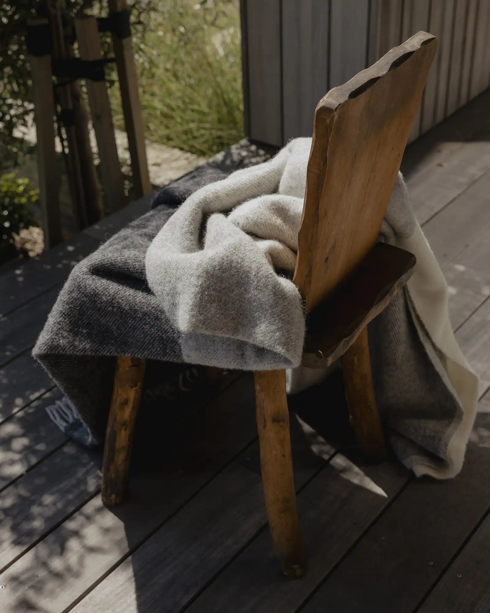 Bayswater Charcoal throw in light grey, dark grey and white, draped over wooden chair on outdoor deck by Weave Home