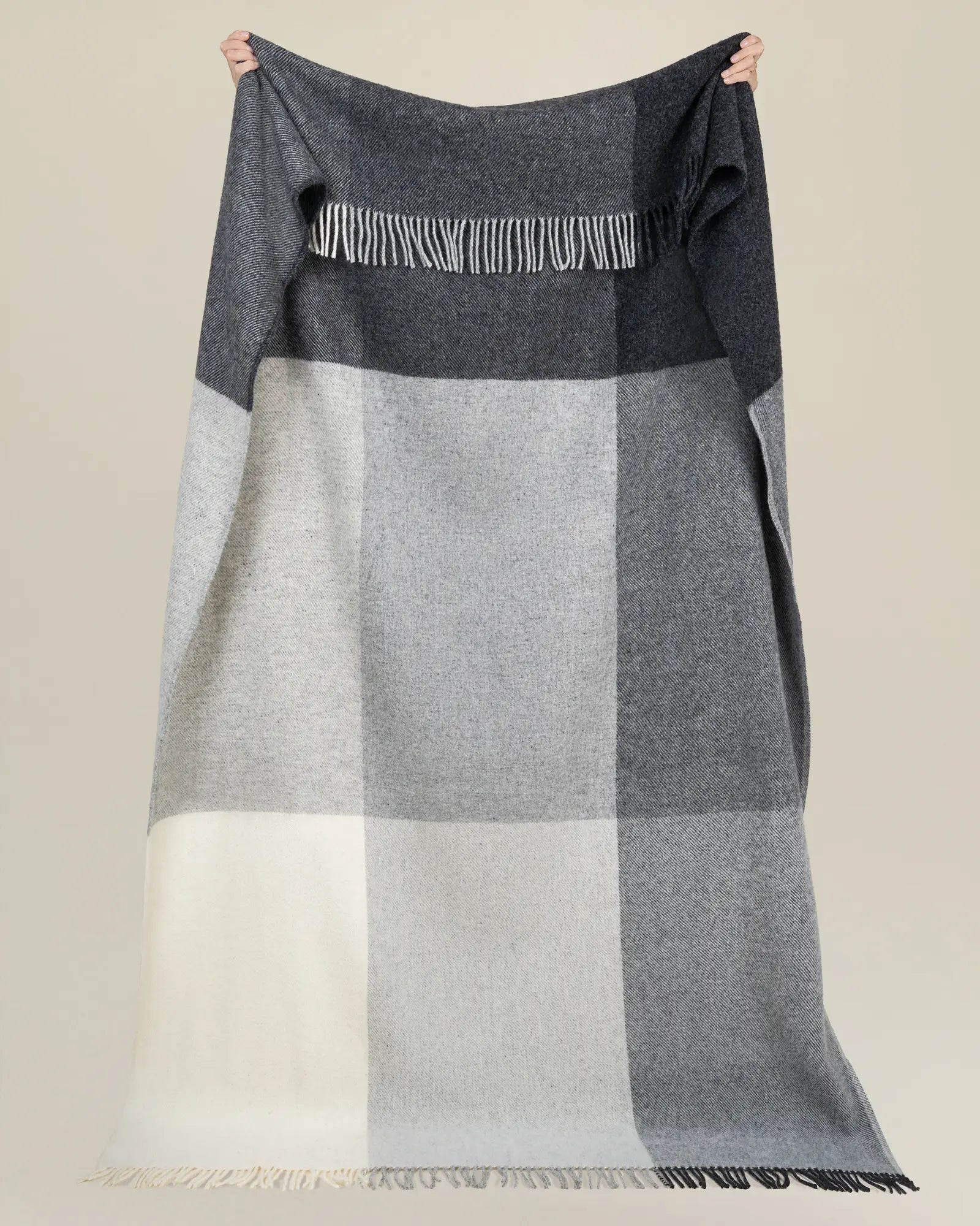 Bayswater Charcoal throw in NZ wool held up to show colour-block pattern with white fringe trim and contrast twill weave bands by Weave Home