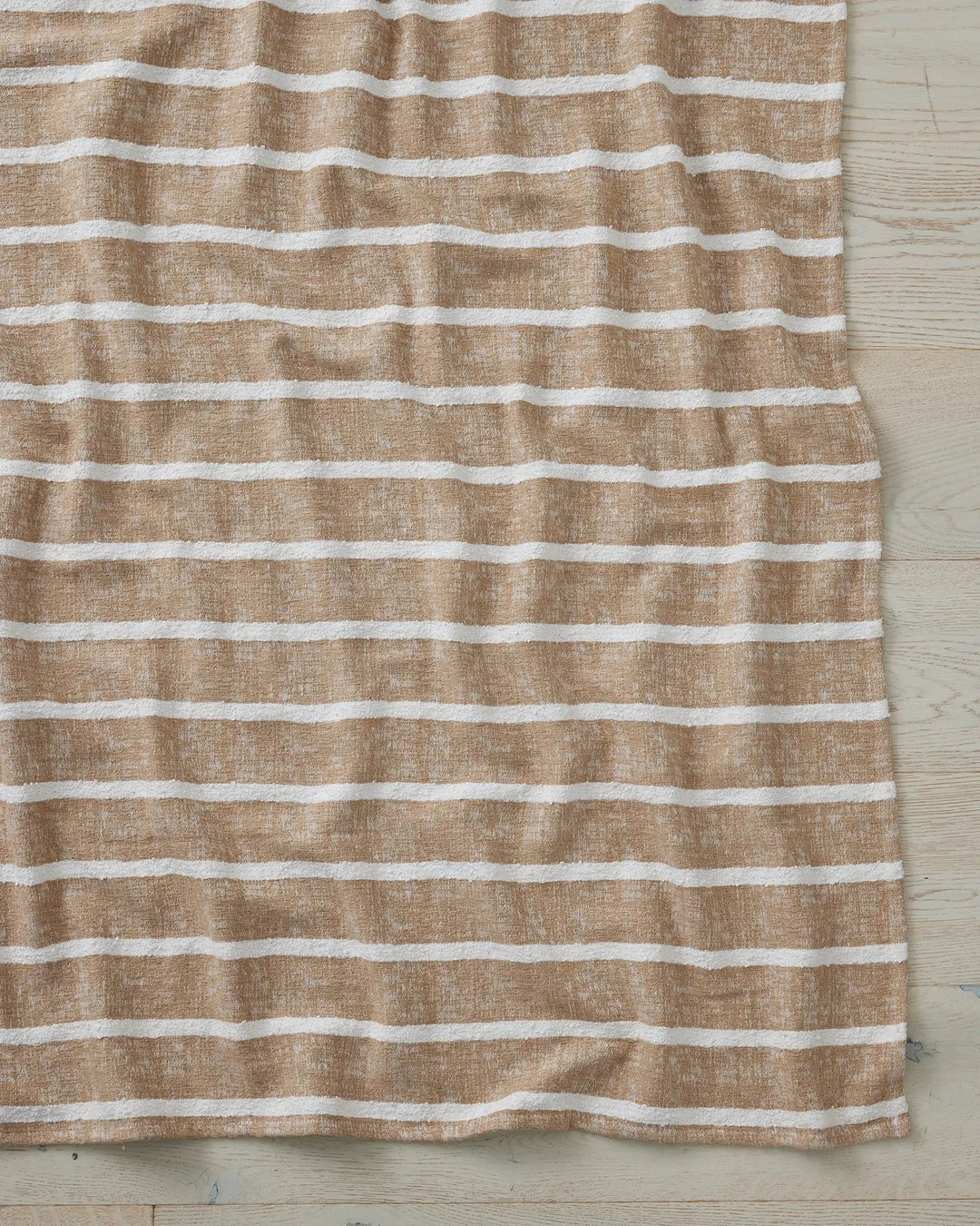 Neutral striped throw in beige and cream with soft linen texture, draped on light wooden flooring in a serene coastal-inspired interior setting